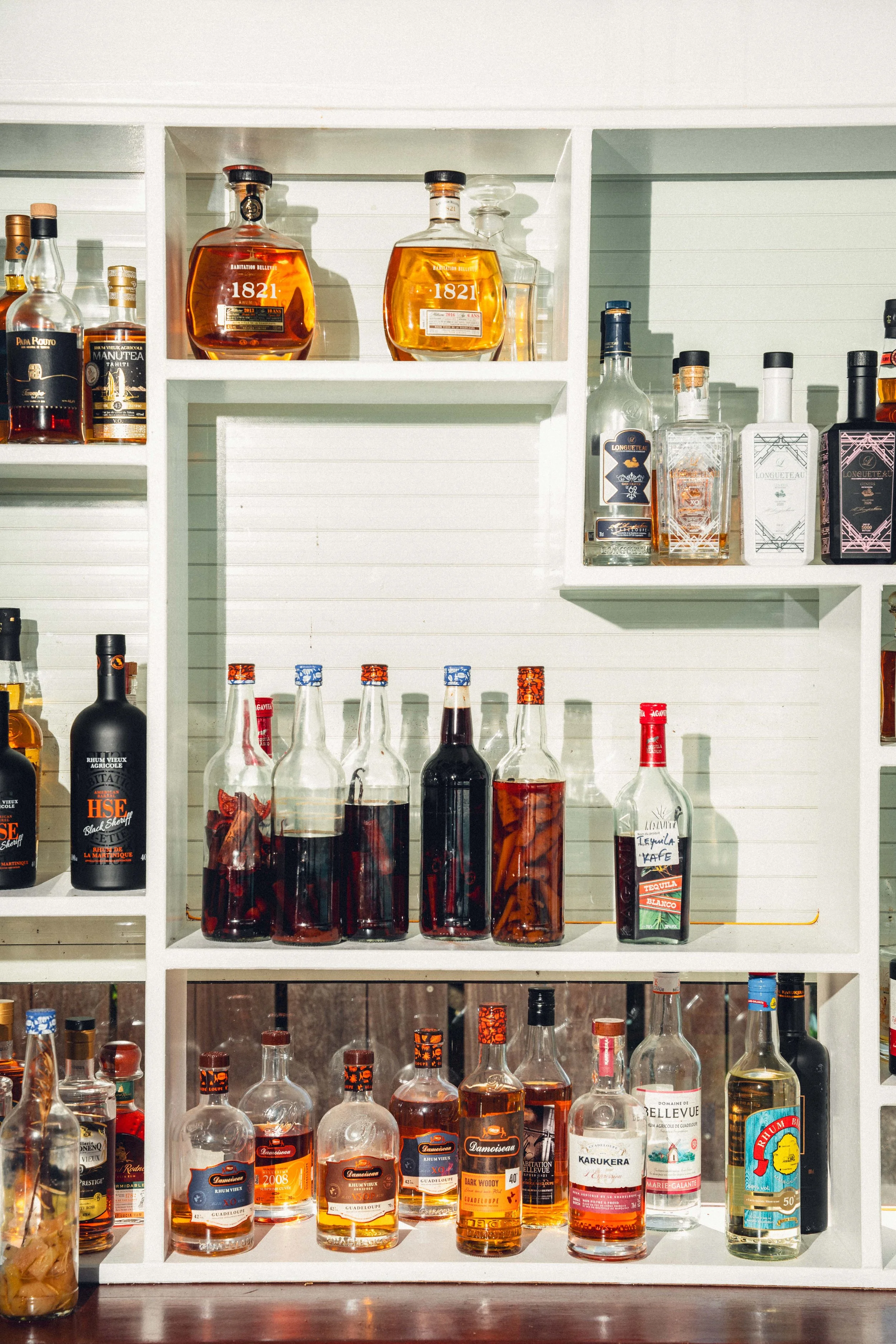Une sélection de bouteilles d'alcool, principalement de rhum, dans une étagère en bois blanche.