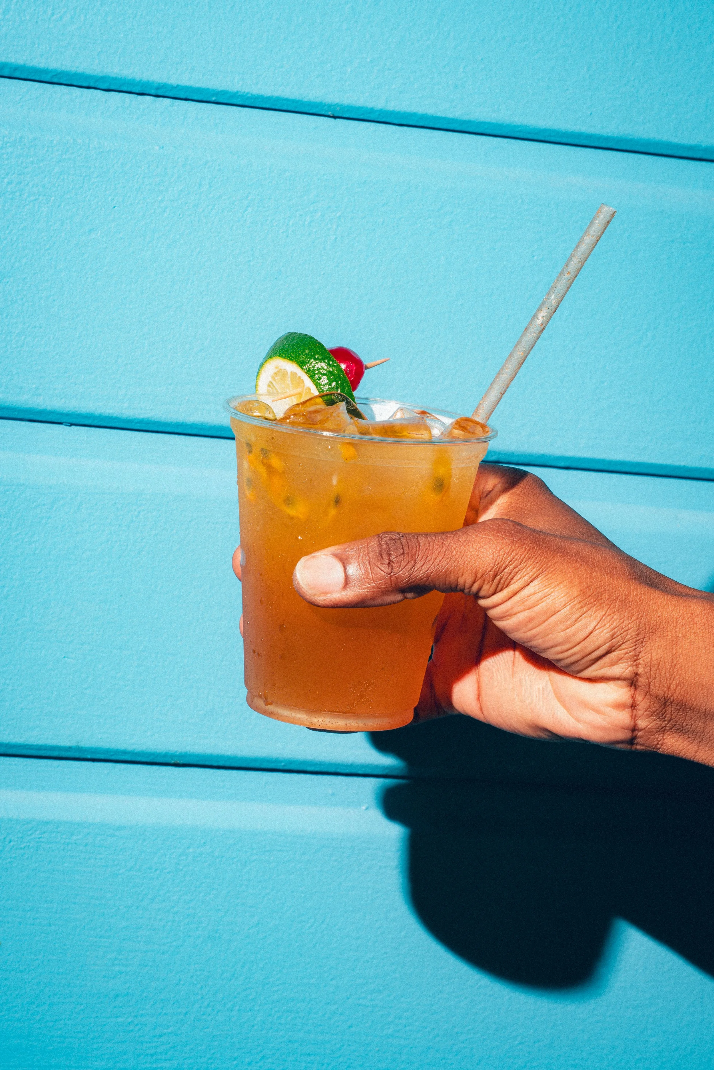 Verre de boisson orange avec une tranche de citron vert, une tranche de citron jaune et une cerise, avec une paille en papier, contre un fond bleu.