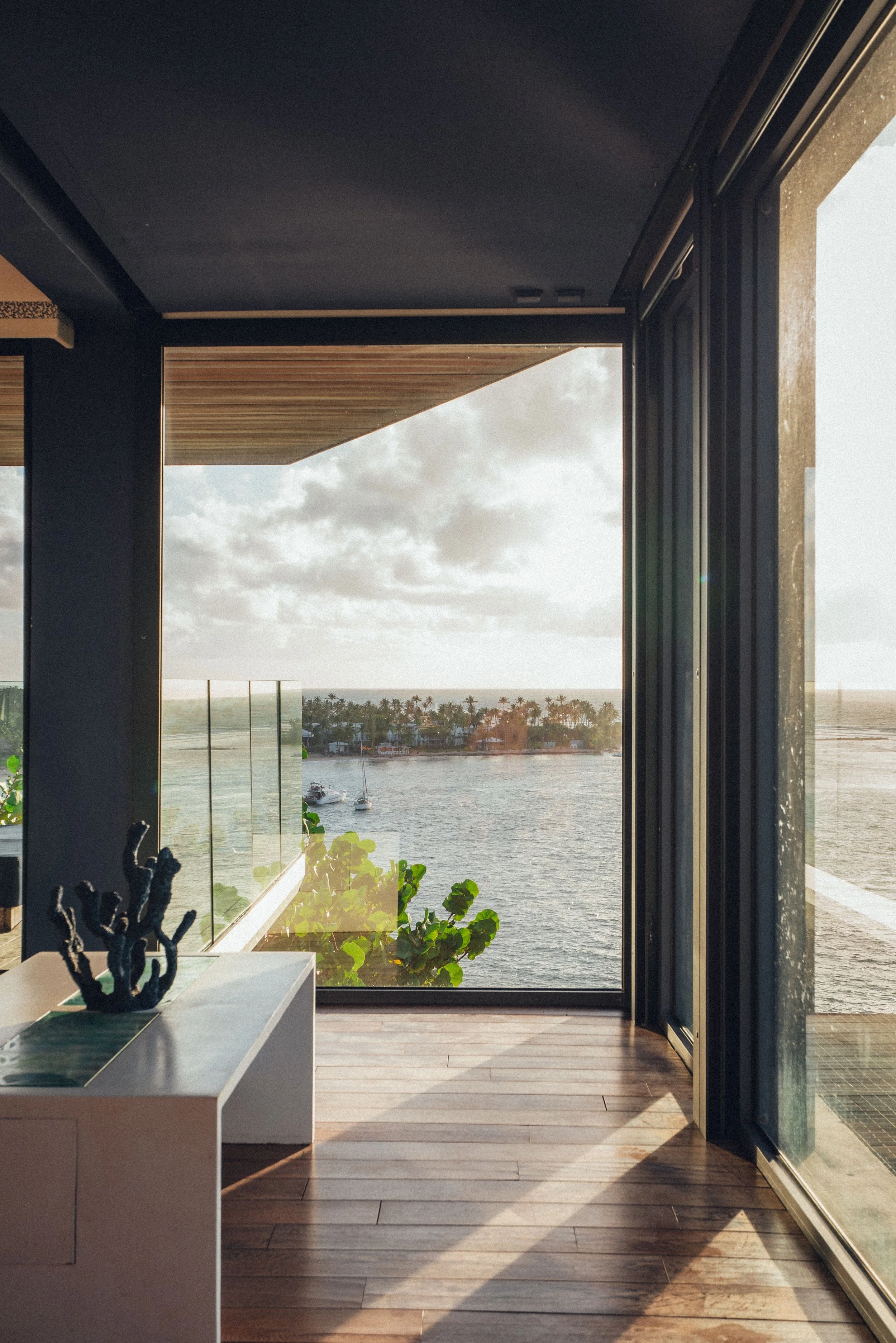 Vue depuis une fenêtre donnant sur une scène maritime avec des cabanons, des palmiers et un bateau, à l'intérieur d'une pièce moderne.