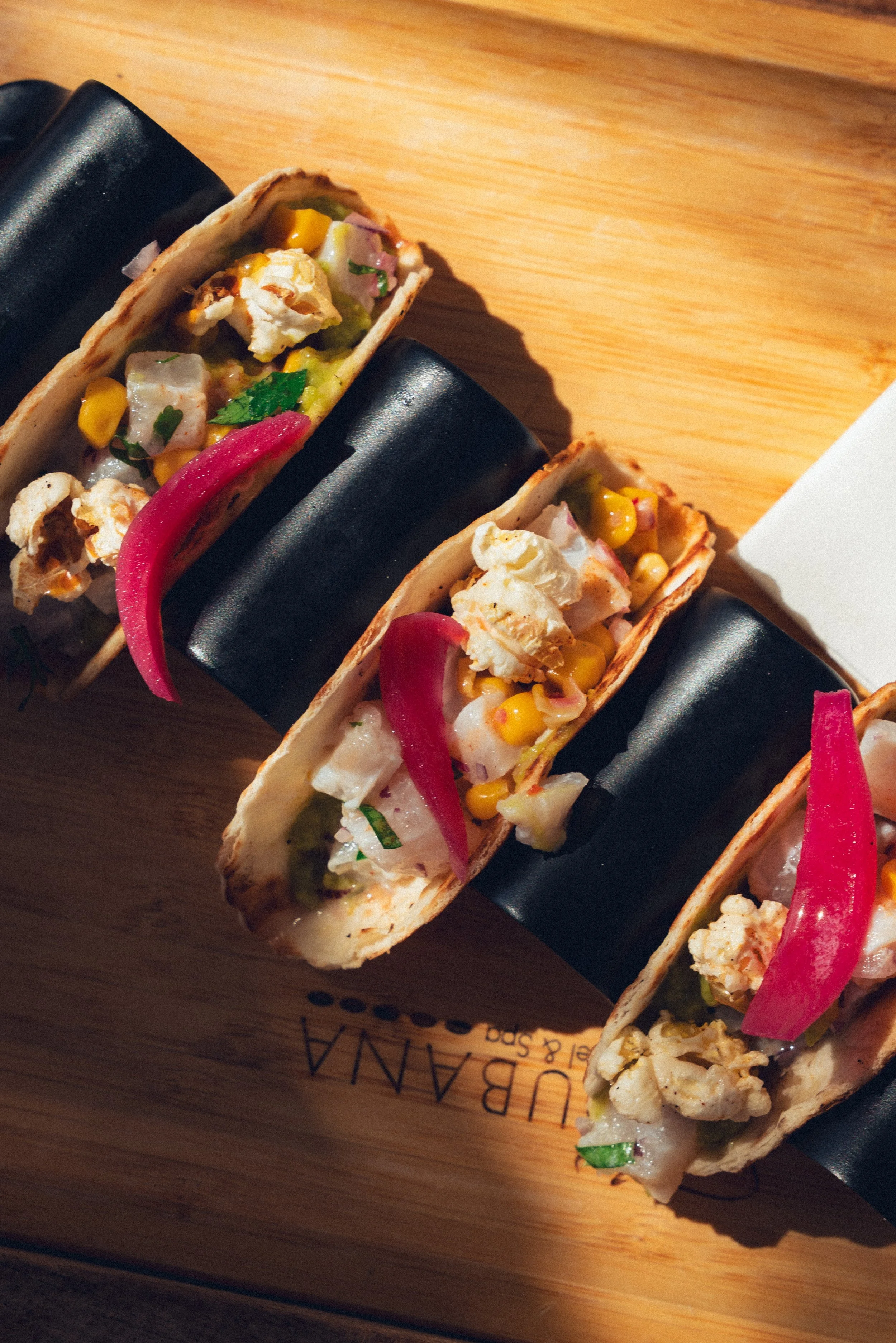Tacos avec légumes, maïs, et garnitures variées sur une assiette en bois.