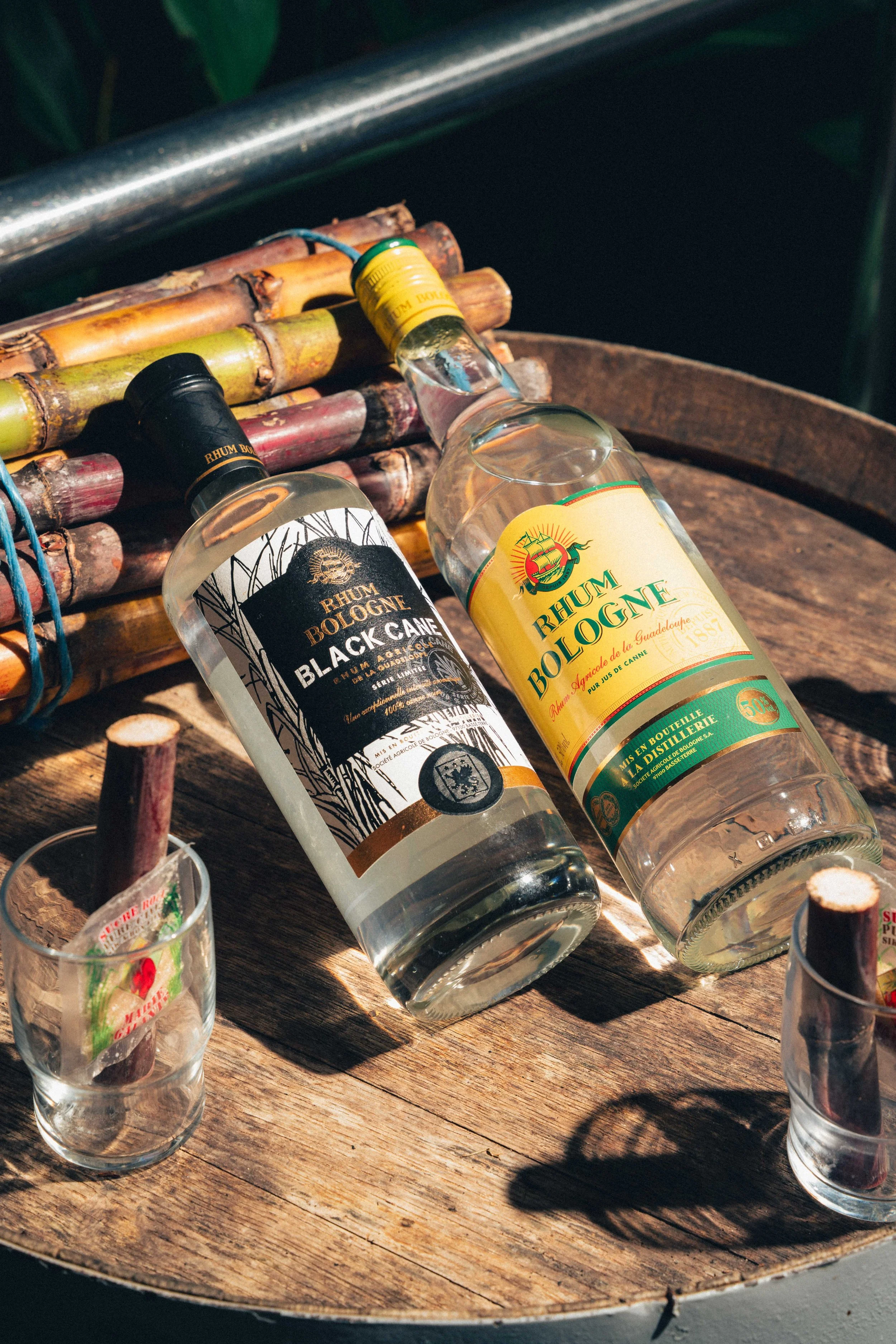 Deux bouteilles de rhum reposent sur une table en bois, entourées de verres en verre, avec un support en bambou derrière elles.