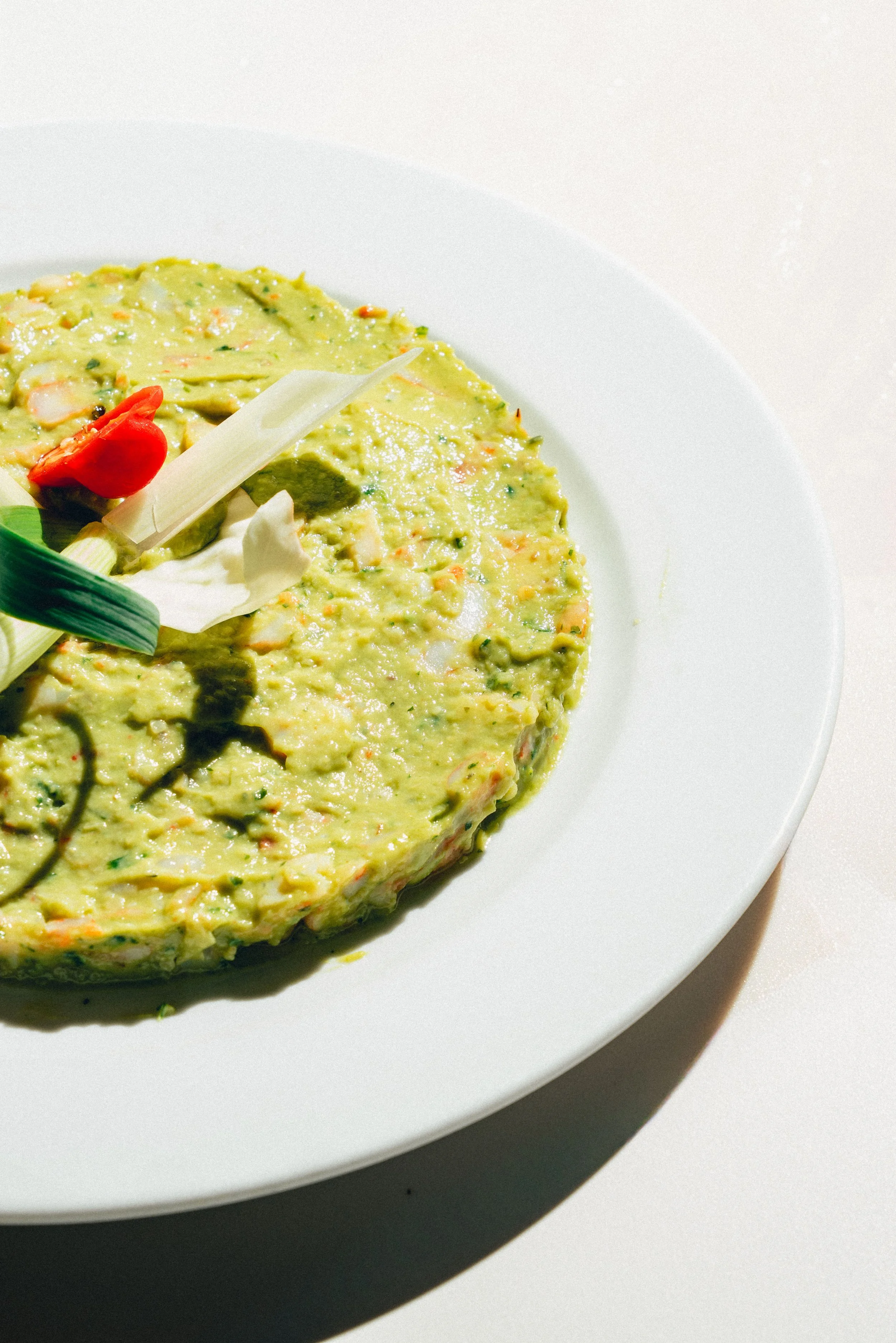 Photographie culinaire d'un plat gastronomique dans un restaurant. Omelette verte garnie de légumes, servie sur une assiette blanche, avec un décor simple.