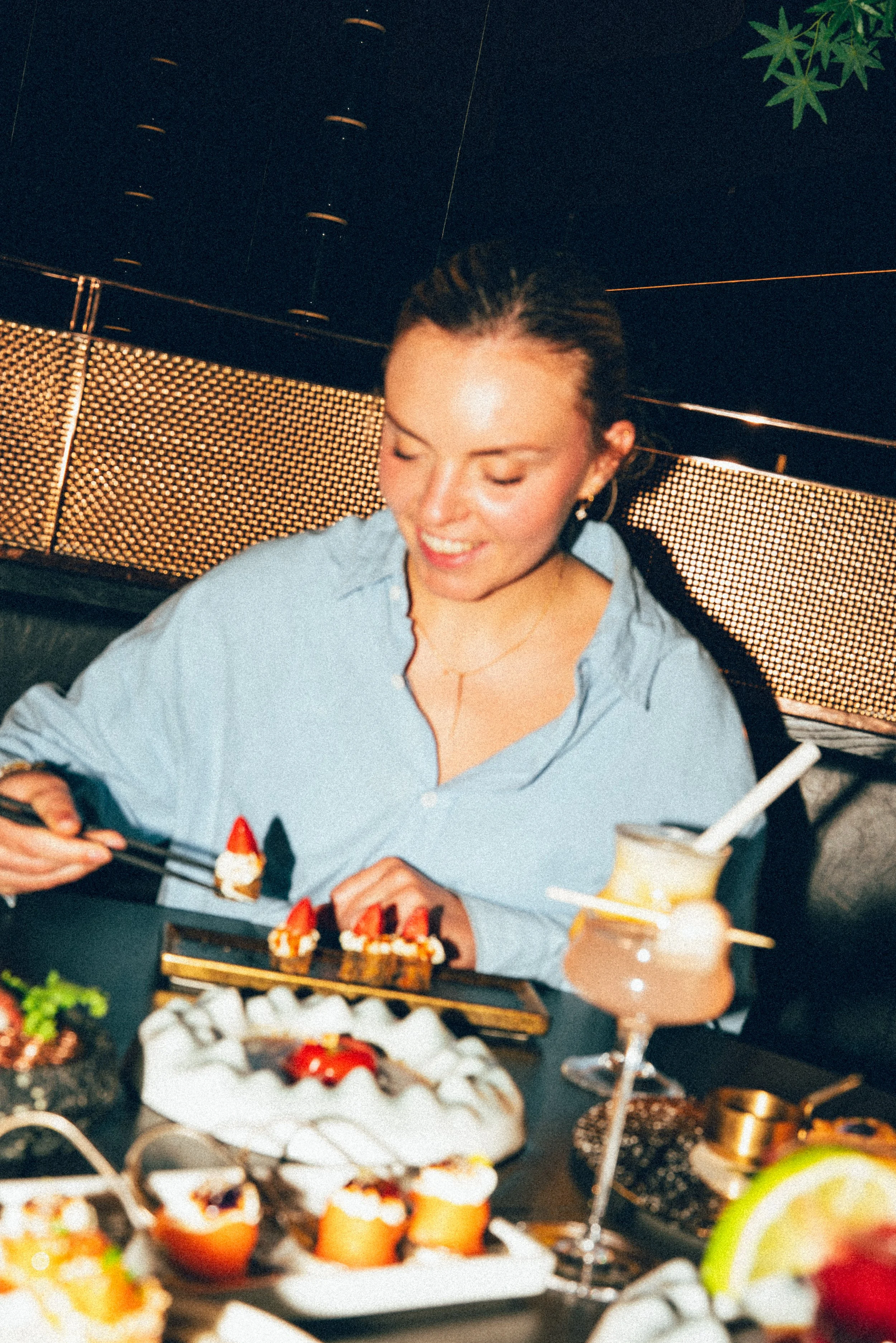 Une femme souriante dégustant des desserts lors d'une fête ou d'un repas, entourée de nombreux desserts et boissons colorés.