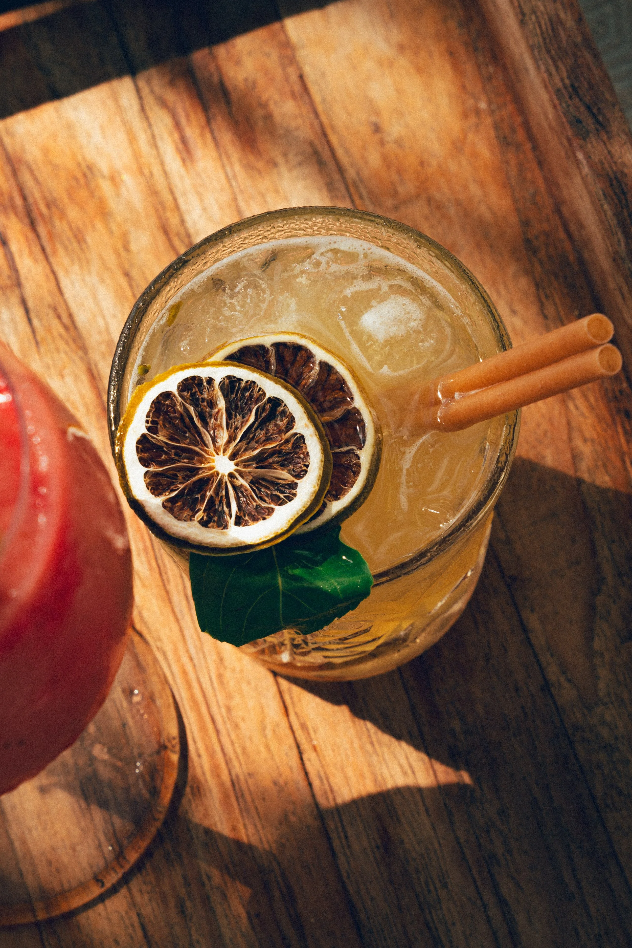 Verre de cocktail avec tranches de citron séchées, deux pailles et une feuille de mint, posé sur une table en bois.
