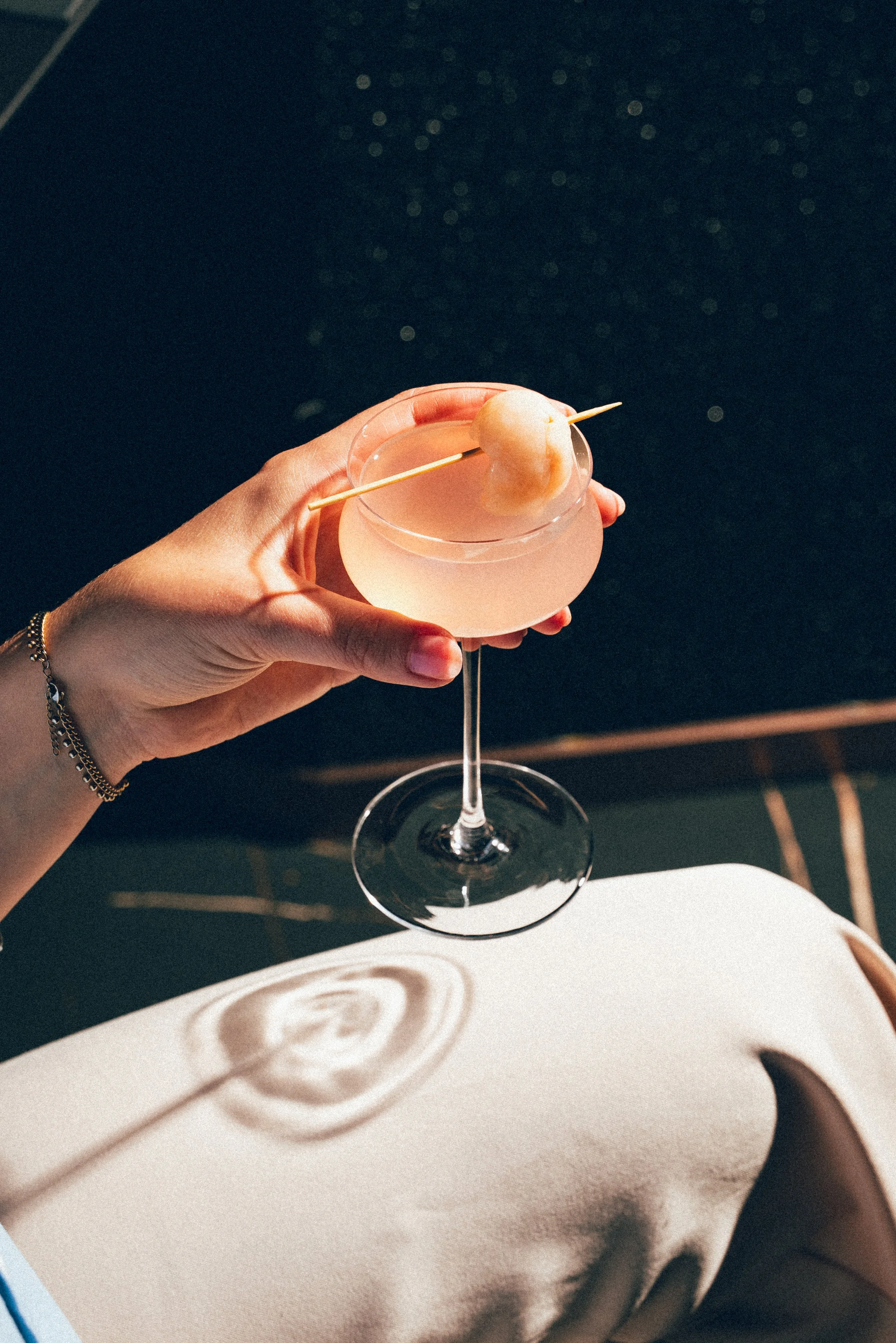 Verre à cocktail rose avec une cerise ou fruit décoratif sur un bâton, placé sur une nappe blanche sous une lumière douce.