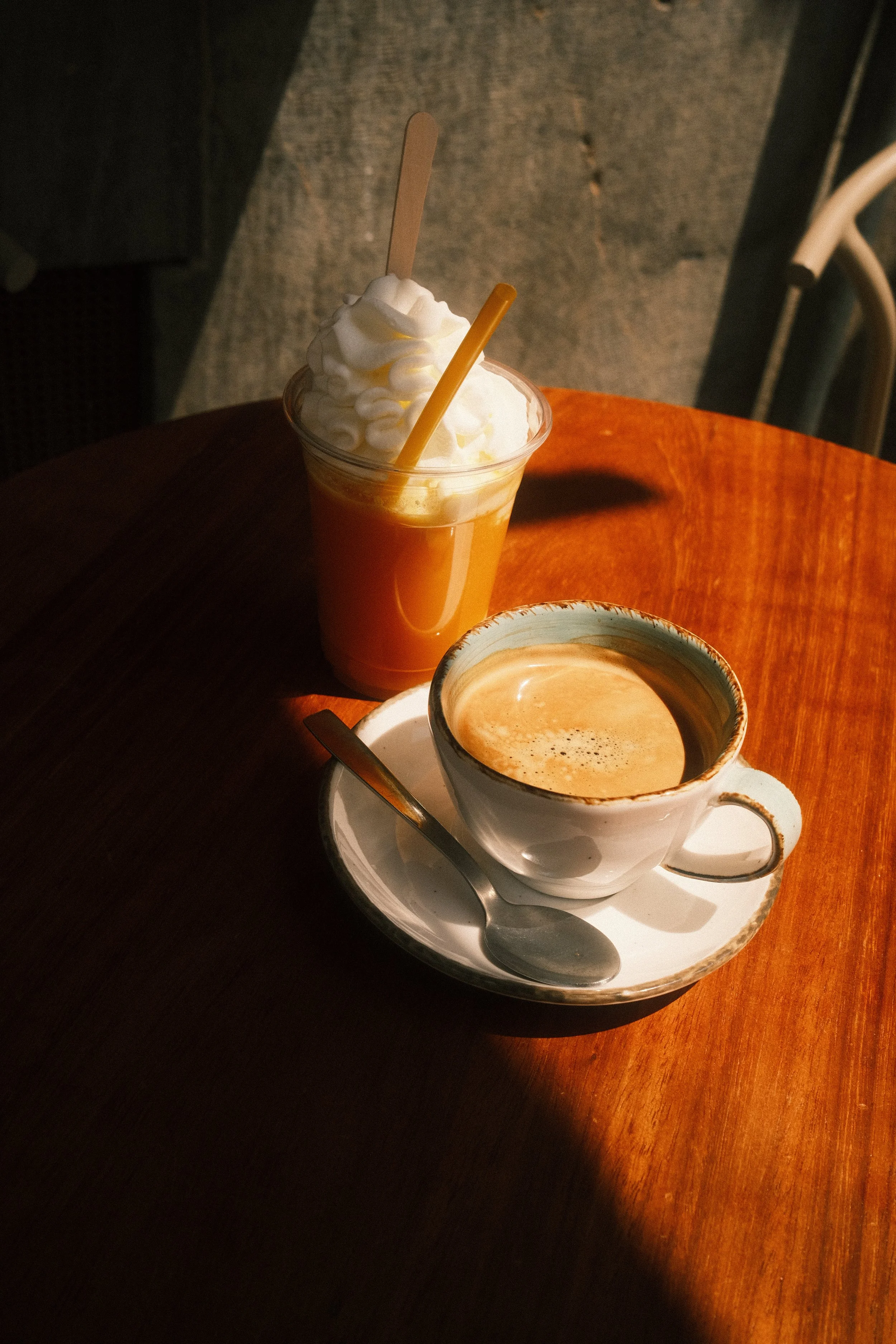 Une tasse de café au lait avec de la mousse, accompagnée d'une cuillère, sur une assiette blanche avec un motif or.