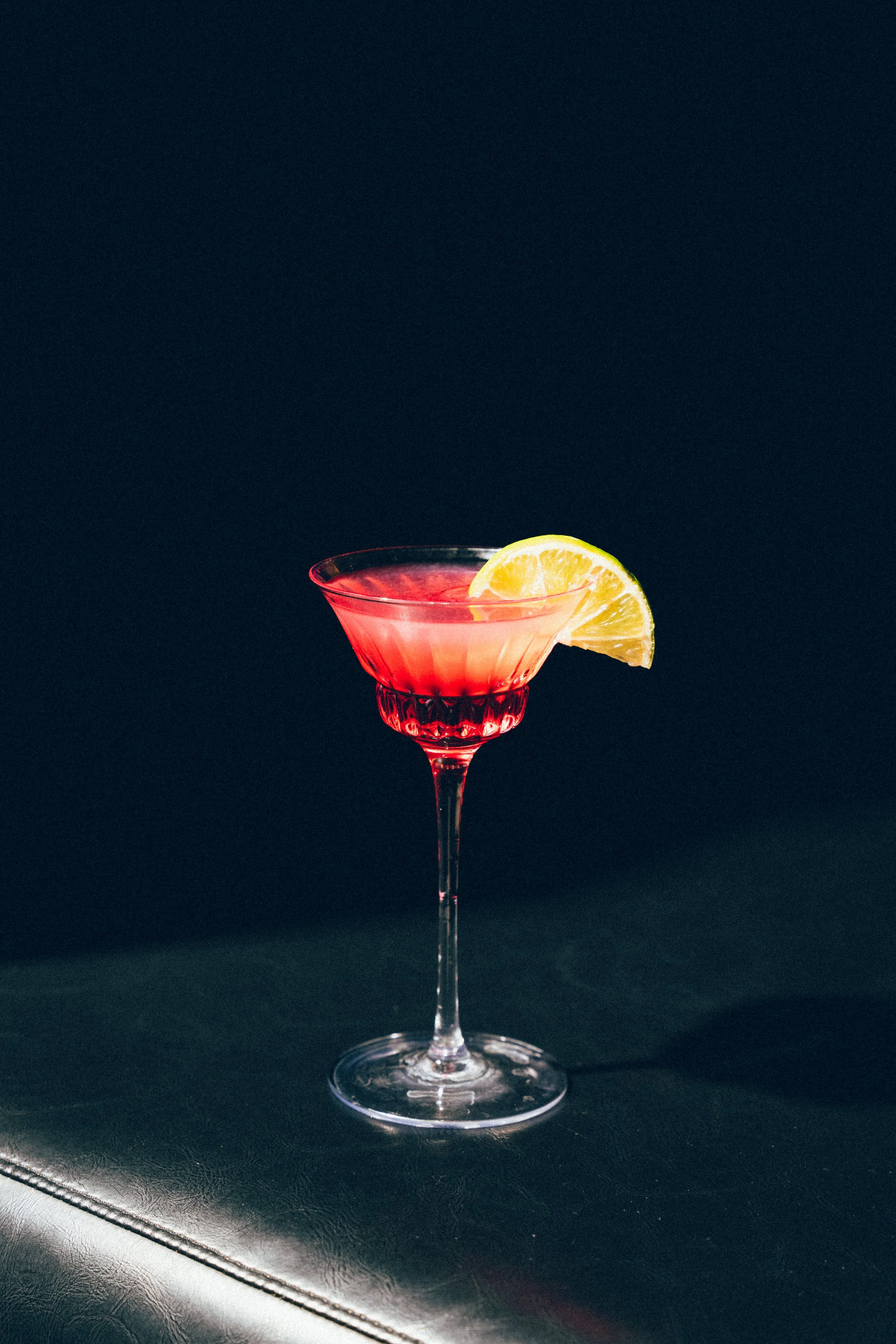 Un verre à cocktail rouge avec une tranche de citron sur le rebord, placé sur une surface noire