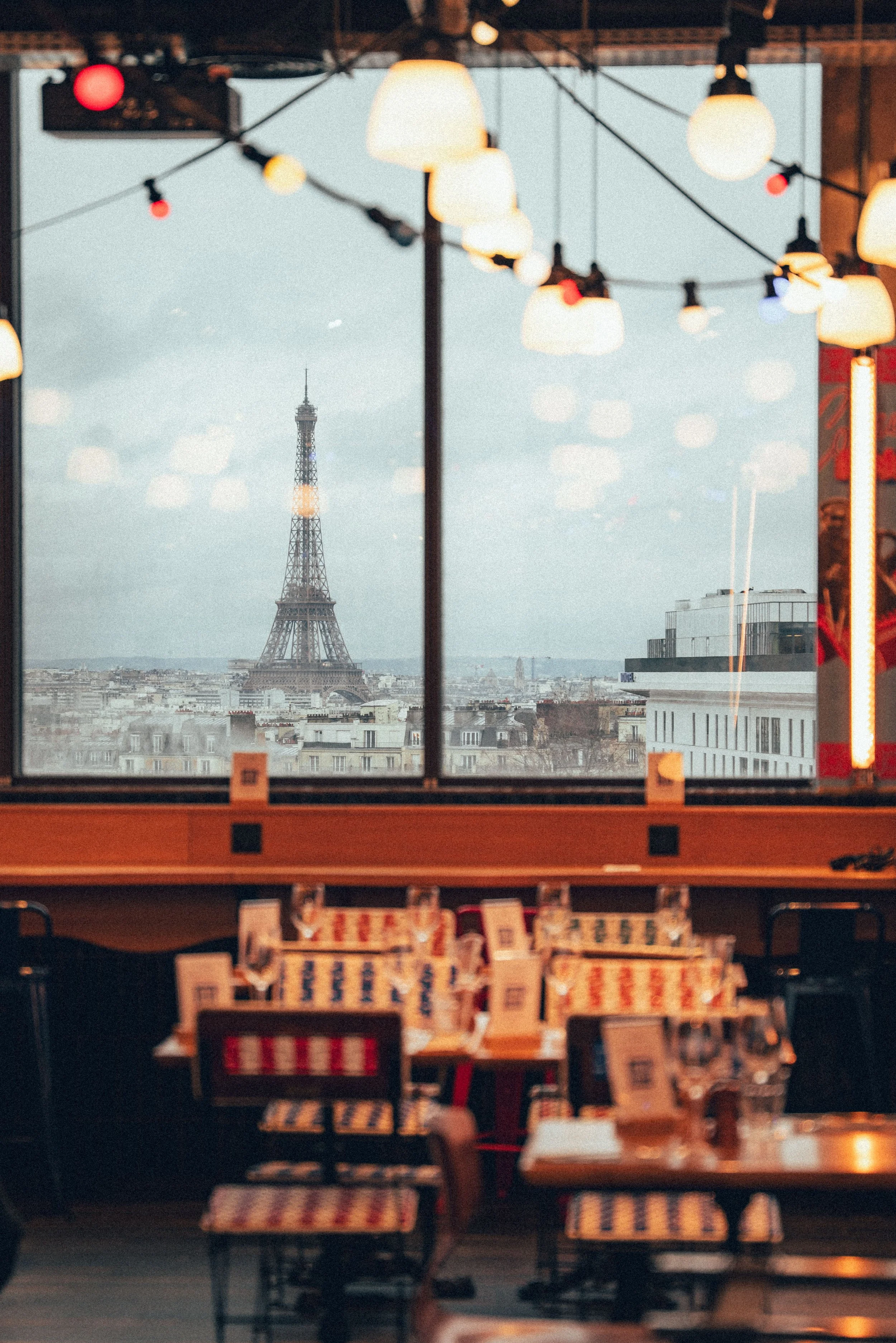 Une vue de Paris avec la tour Eiffel visible à travers une grande fenêtre dans un café ou une librairie, éclairée par des lampes suspendues