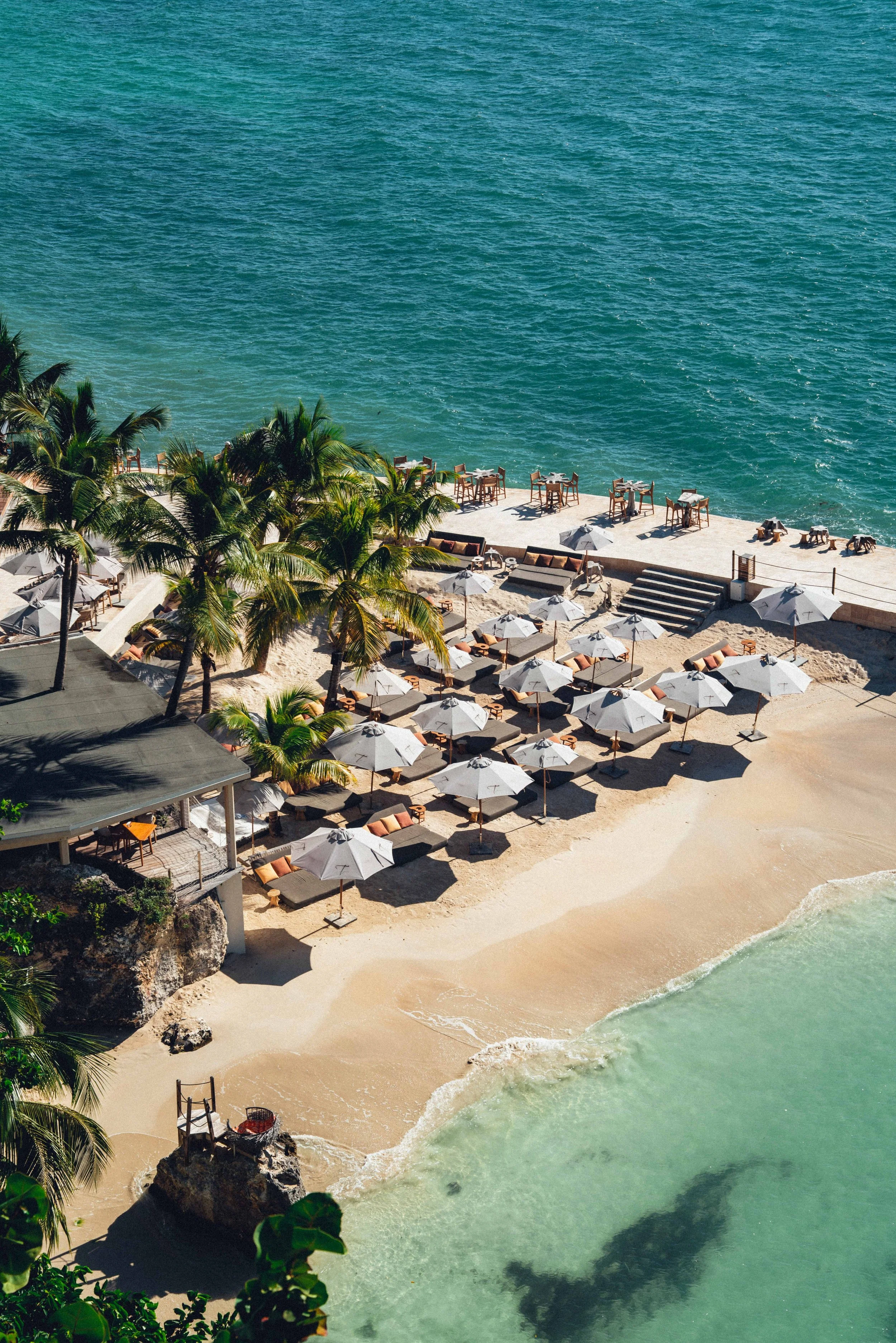 Plage de sable avec parasols et chaises longues, palmiers, et l'océan turquoise