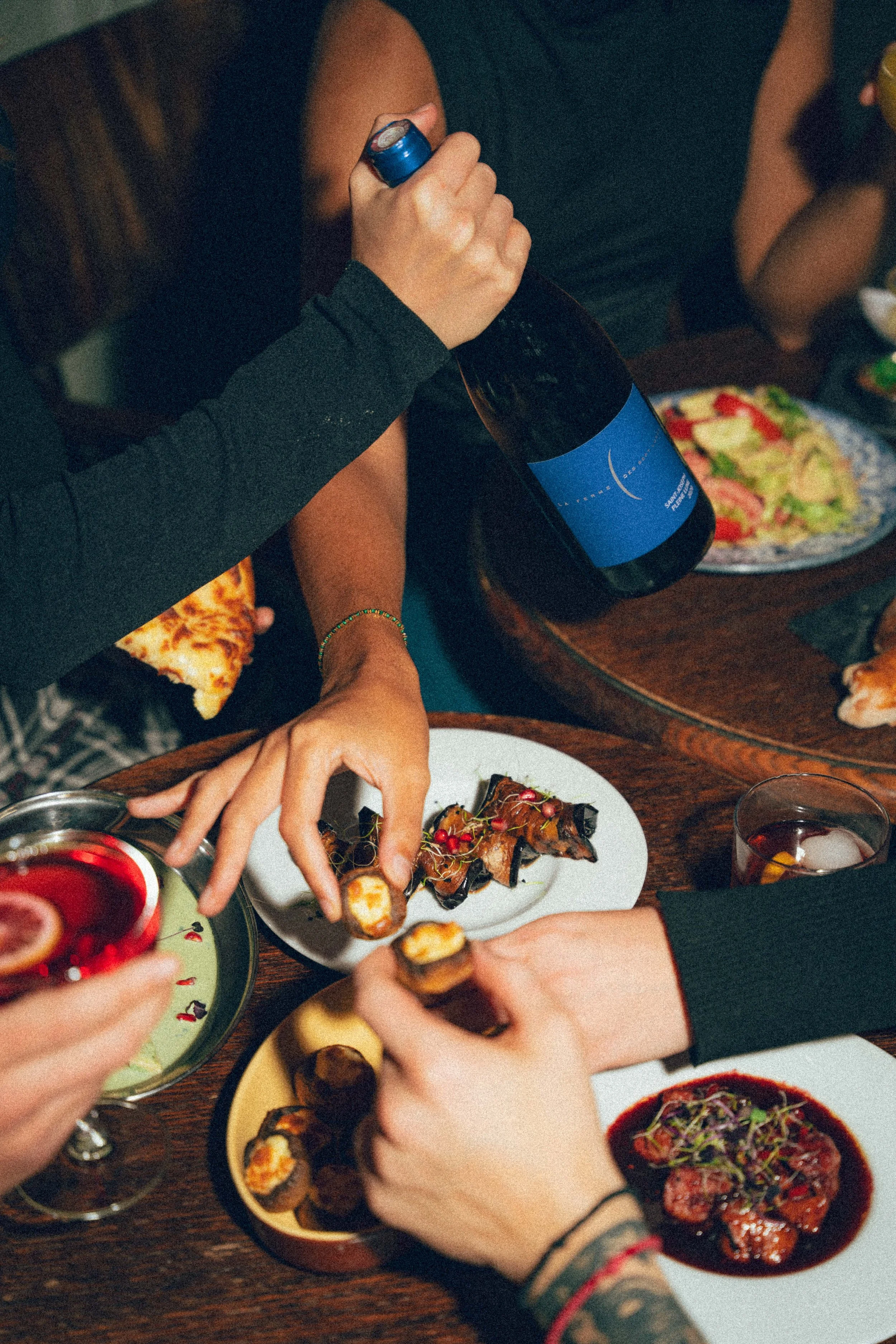 Groupe de personnes partageant un repas avec des sushis, des plats, des boissons et un vin lors d'une réunion conviviale.
