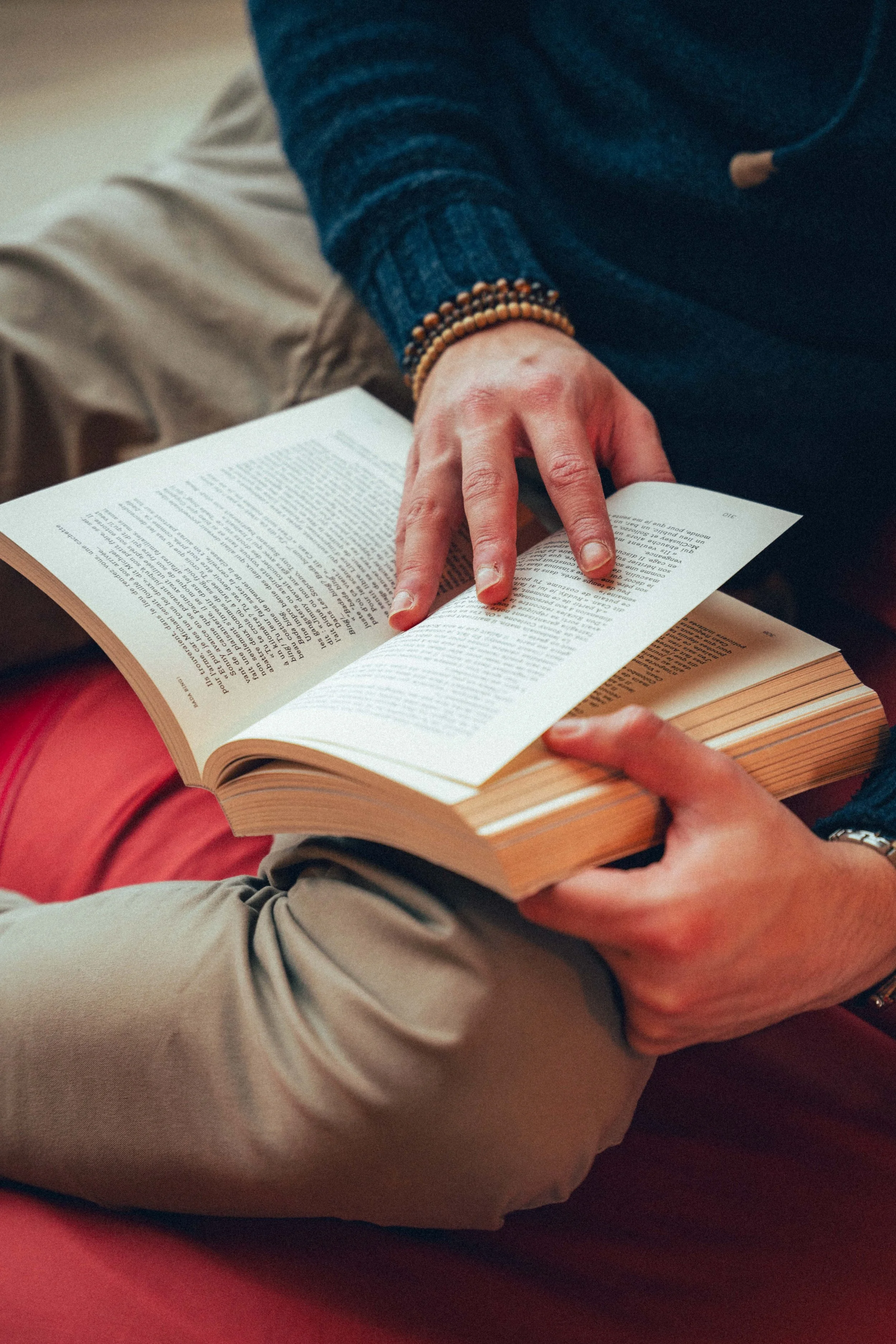 Deux personnes lisent un livre ensemble. L'une d'elles porte un bracelet de perles et une veste bleue. La scène est intime et détendue.