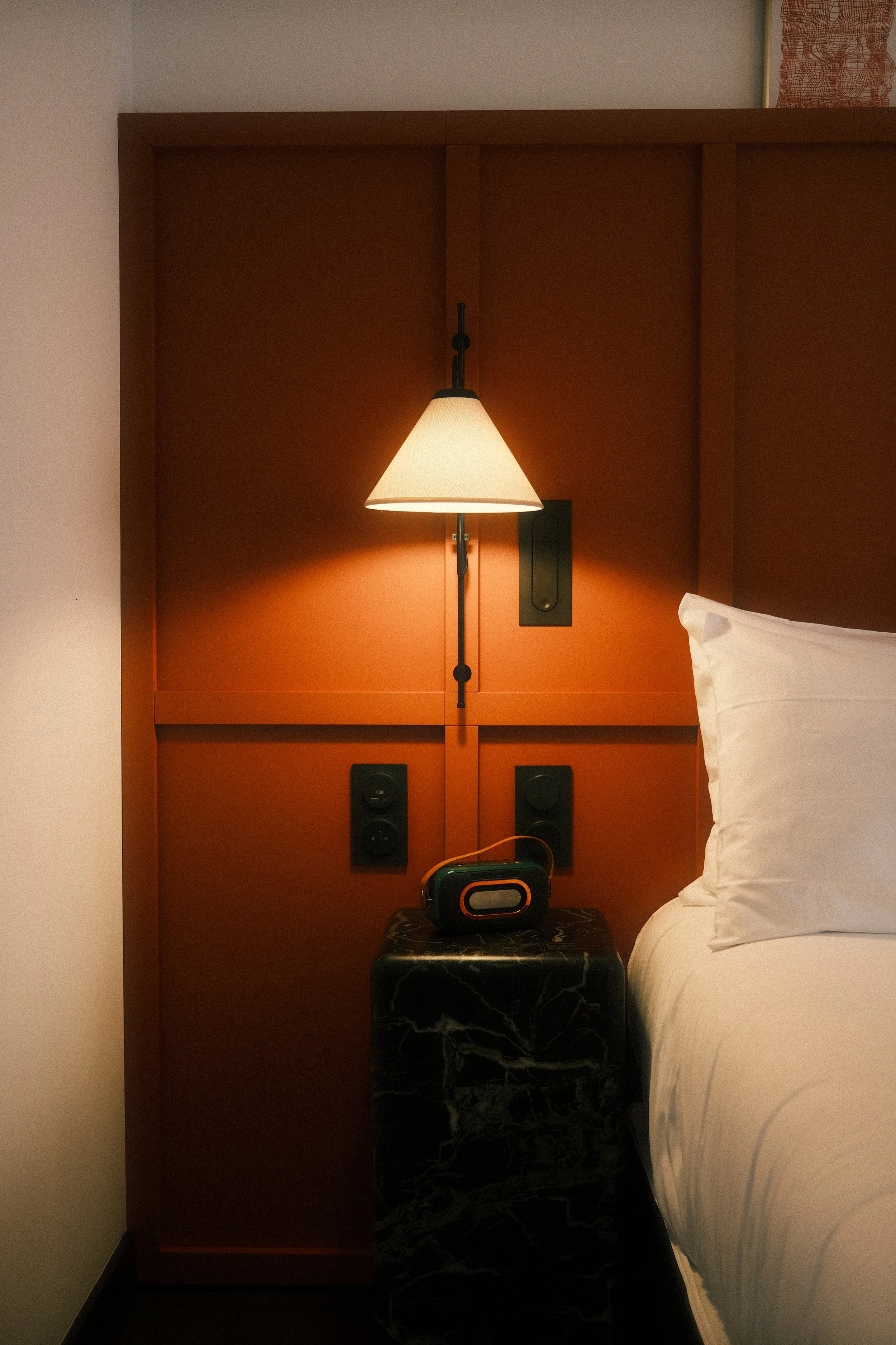 Lampe de chevet allumée, étendue sur une table de nuit en marbre noir dans une chambre avec un lit à côté.
