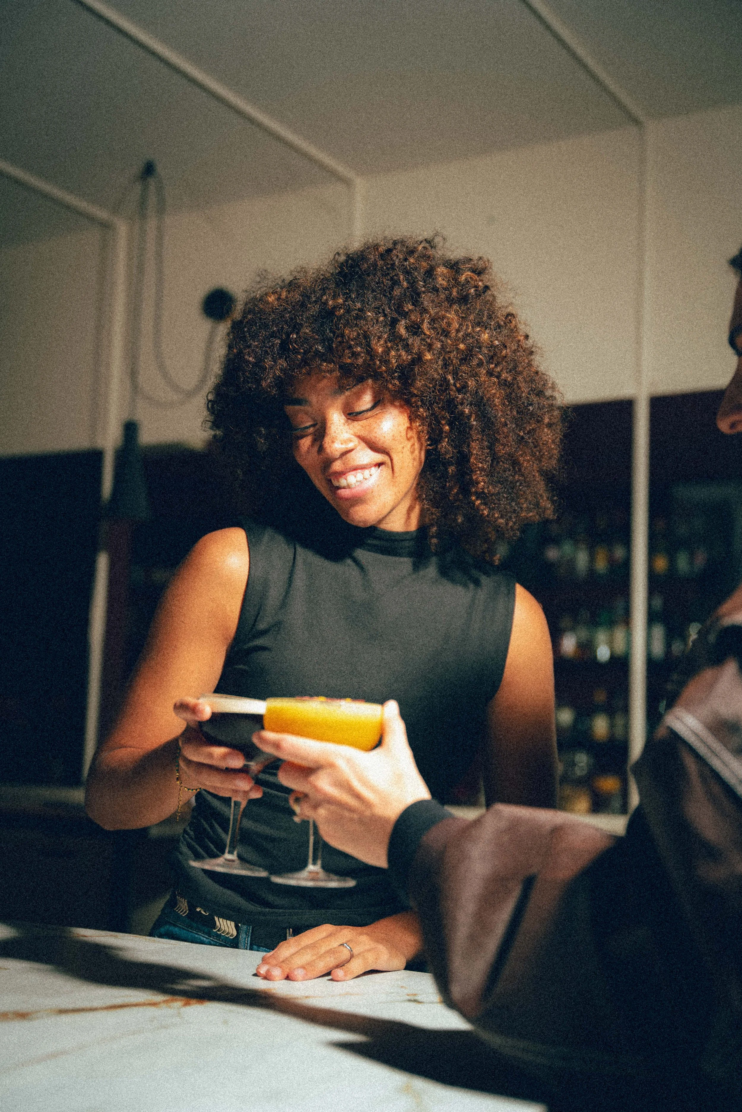 Une femme souriante en train de recevoir un verre de cocktail lors d'une soirée.