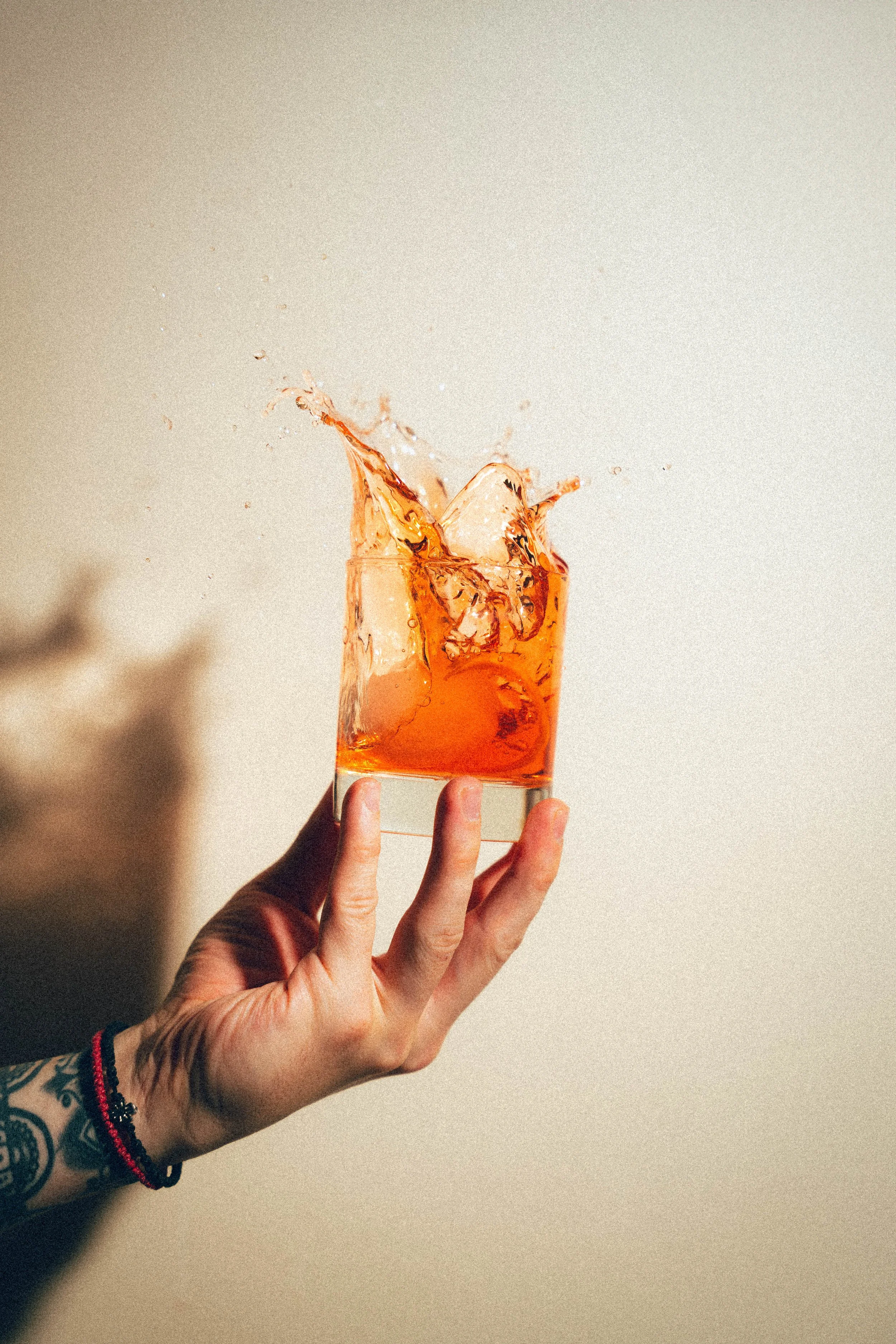 Une main tient un verre transparent rempli d'une boisson orange avec des glaçons, la boisson et le verre éclabousent en raison d'un geste brusque.