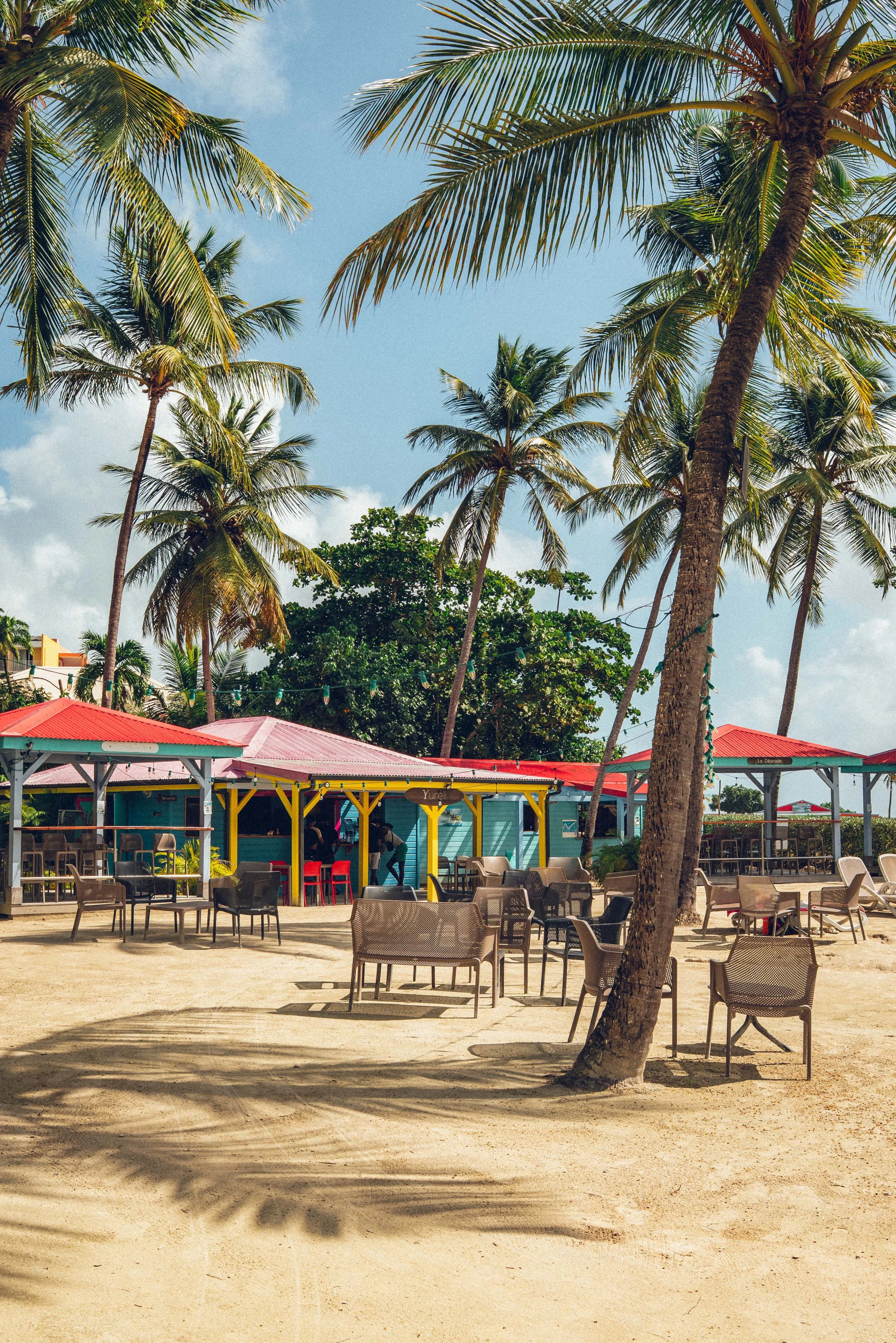 Plage avec des palmiers, des chaises et des kiosques colorés.