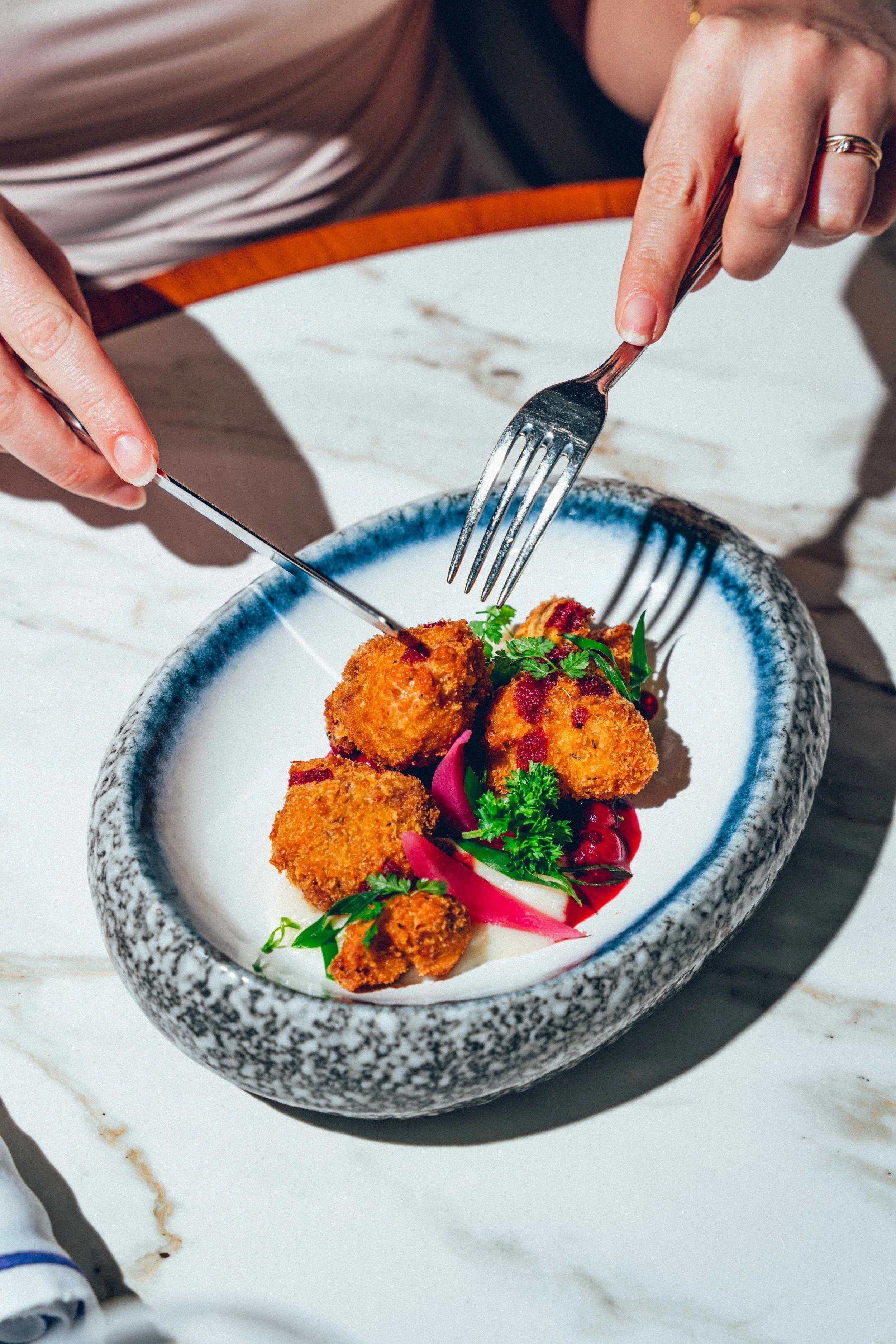 Photographie culinaire d'un plat gastronomique avec des croquettes frites, garniture de légumes et herbes fraîches, sur une table en marbre blanc.