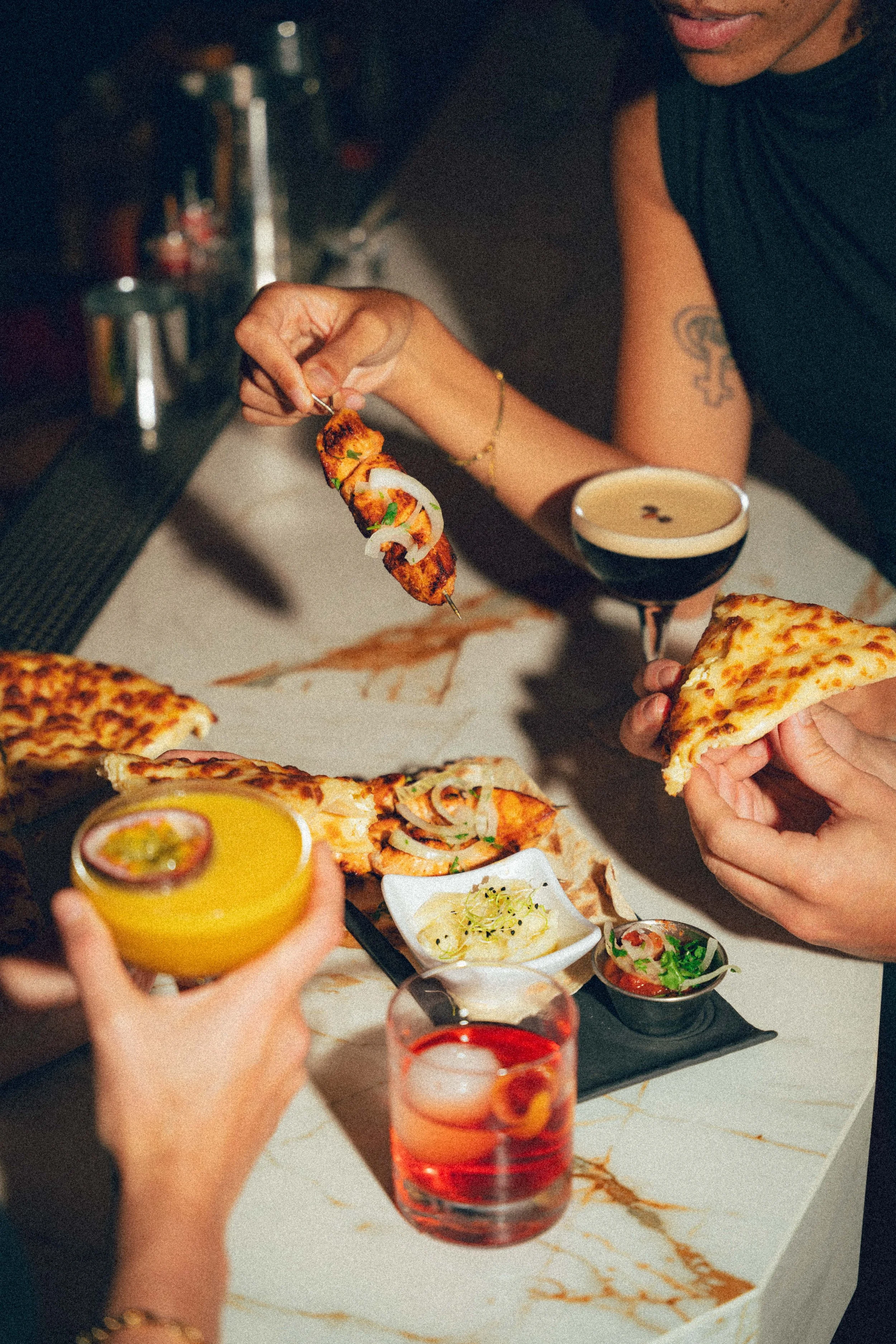 Groupe de personnes dégustant des plats de pizza, accompagnés de cocktails colorés, dans un restaurant ou bar.