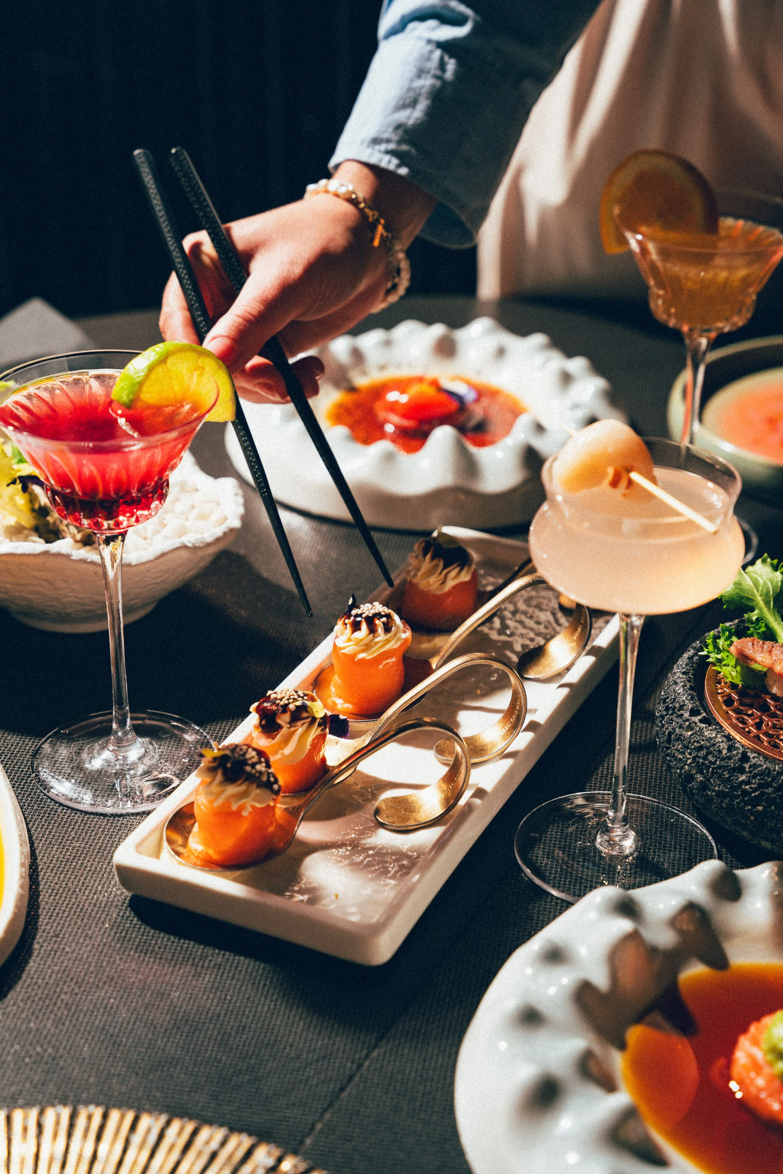 Une table avec des cocktails colorés, des desserts et des plats, des mains d'une personne qui sert une boisson