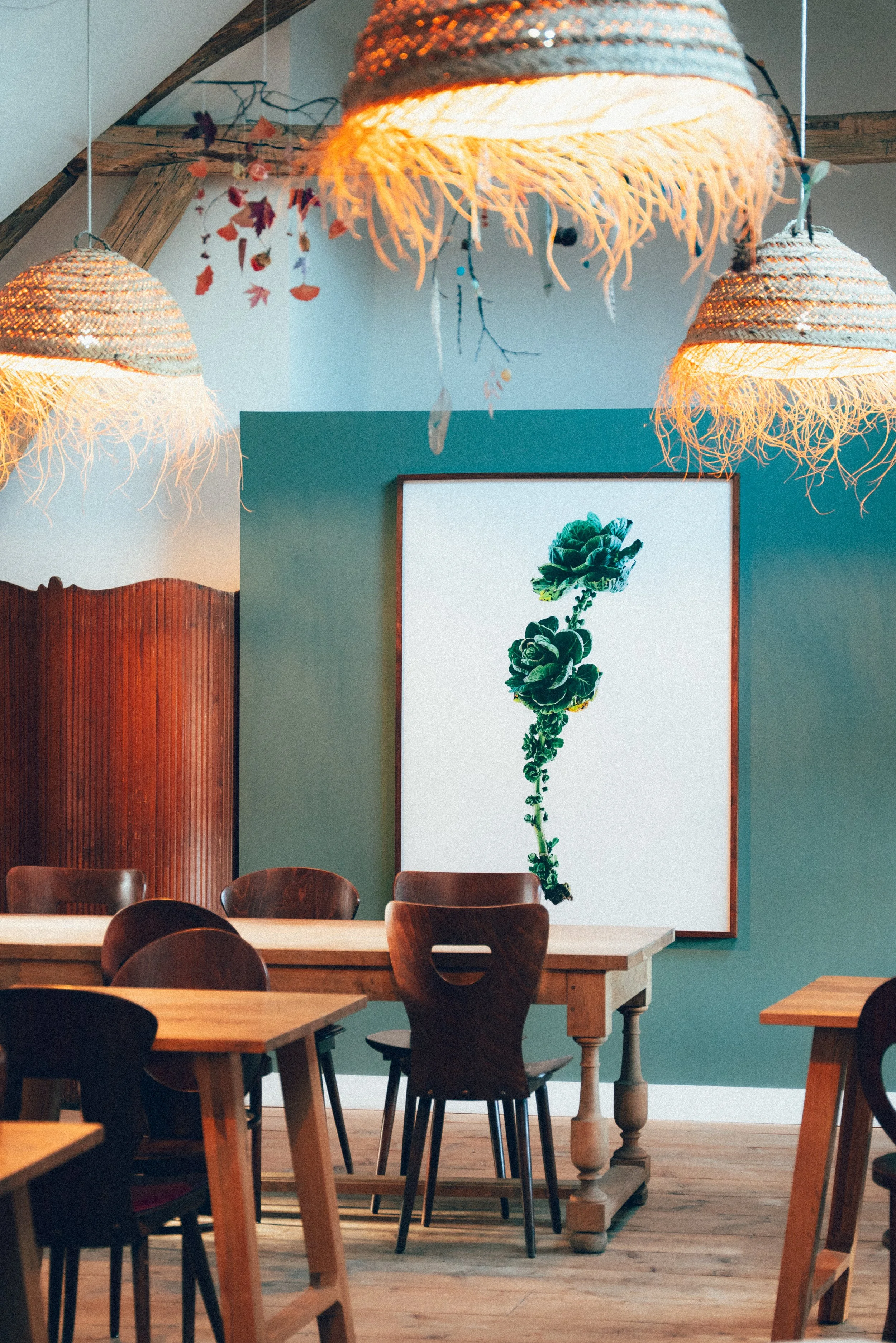 Intérieur d'un café avec un mur vert, un tableau représentant une brocoli, plusieurs tables en bois et des chaises en bois.
