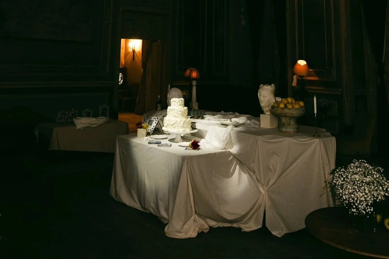 Mesa de casamento com bolo, flores, esculturas e velas em ambiente escuro