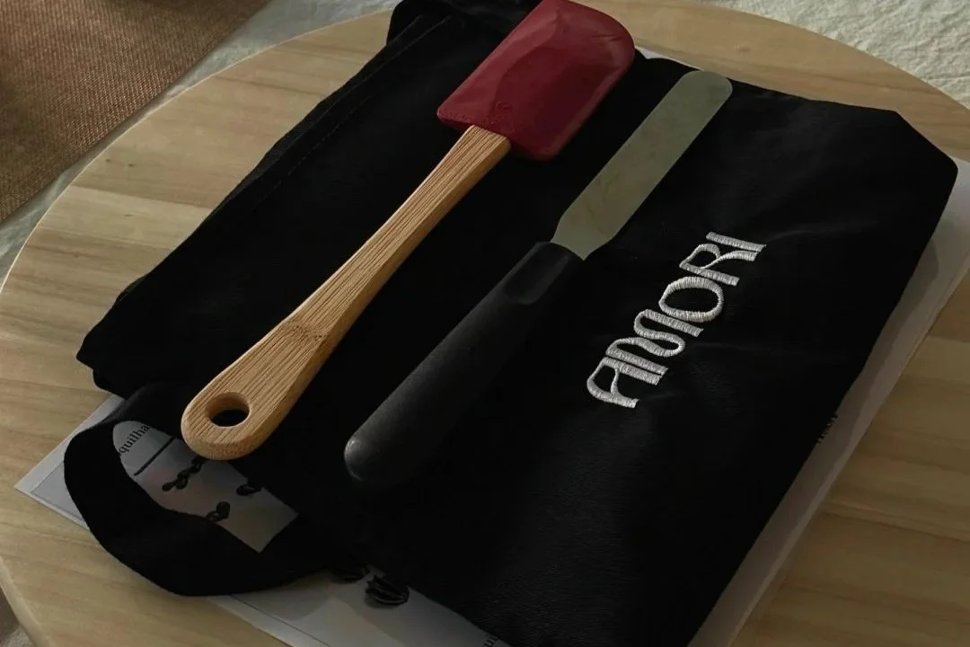 Mesa de madeira com ferramentas e utensílios para usar no workshop: espátulas, aventais e folhas de treino.