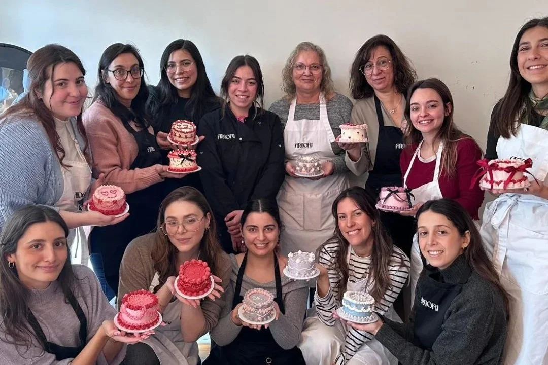 Grupo de mulheres a sorrir enquanto seguram os seus bolos decorados durante o workshop.