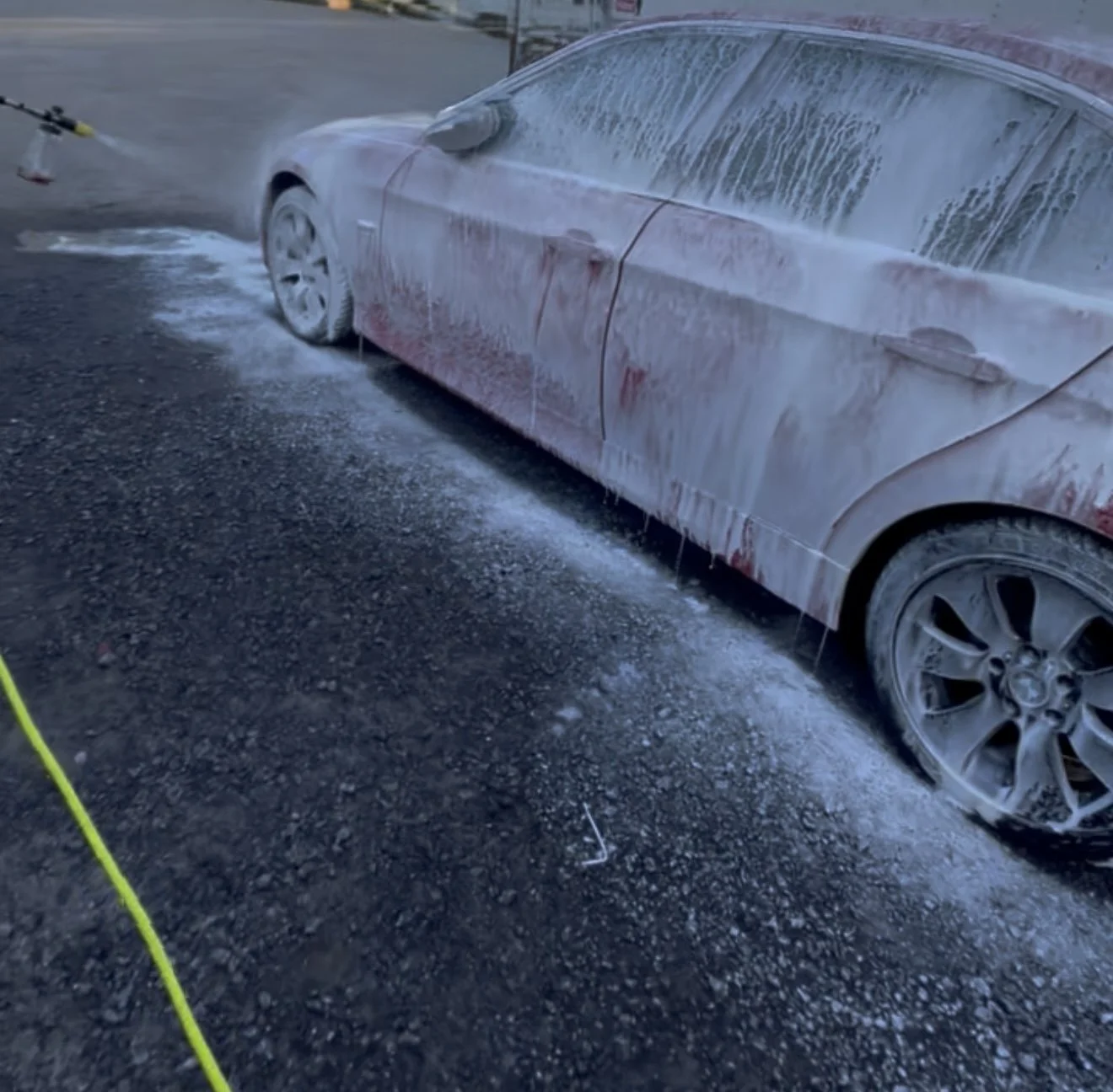 A bright red BMW sedan being treated with a thick snow foam pre-wash at Results Detailing and Pressure Washing in Cayuga Heights, NY.