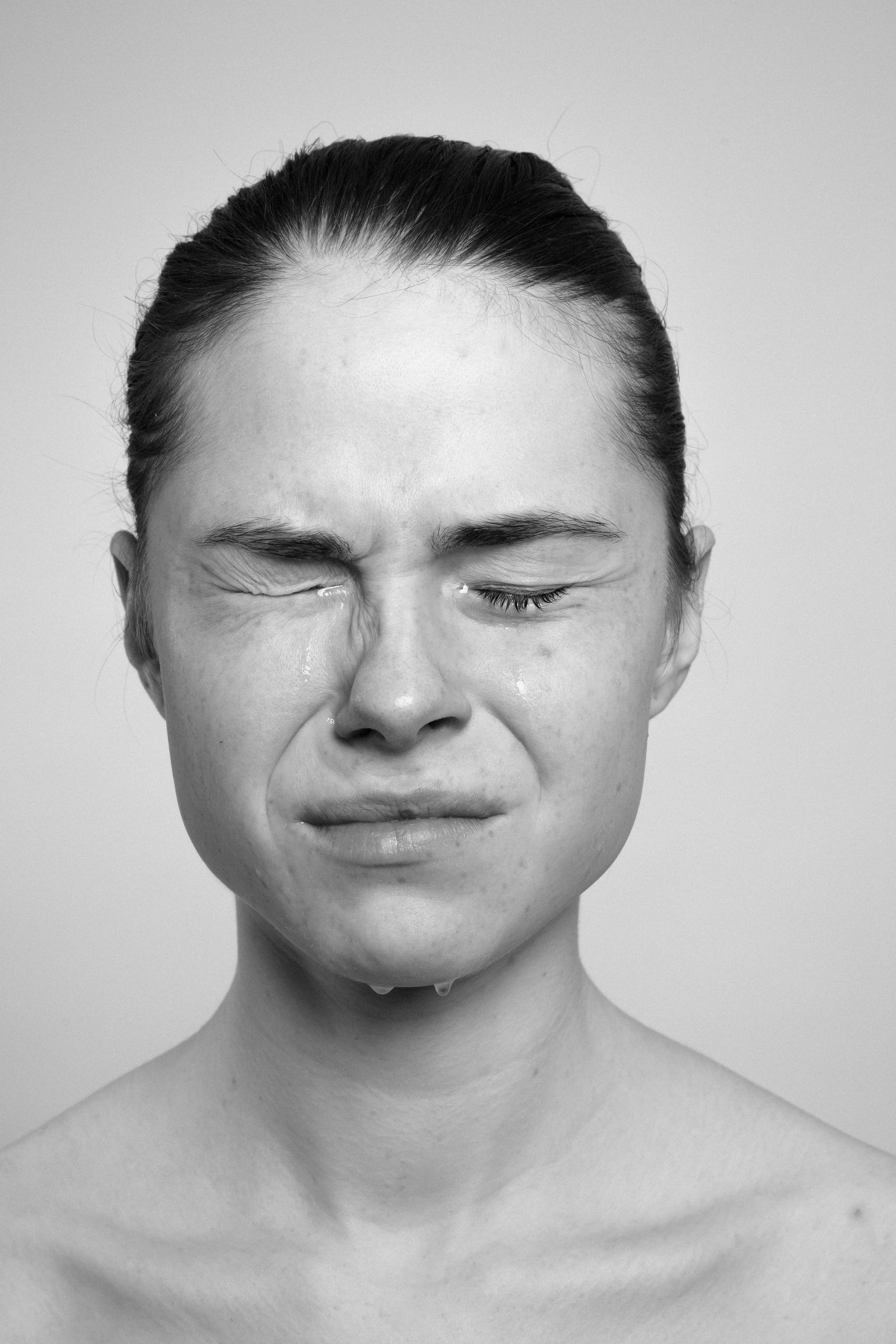 Studio portrait of a young woman in black and white. She frowns, makes faces, grimaces, as if in pain.