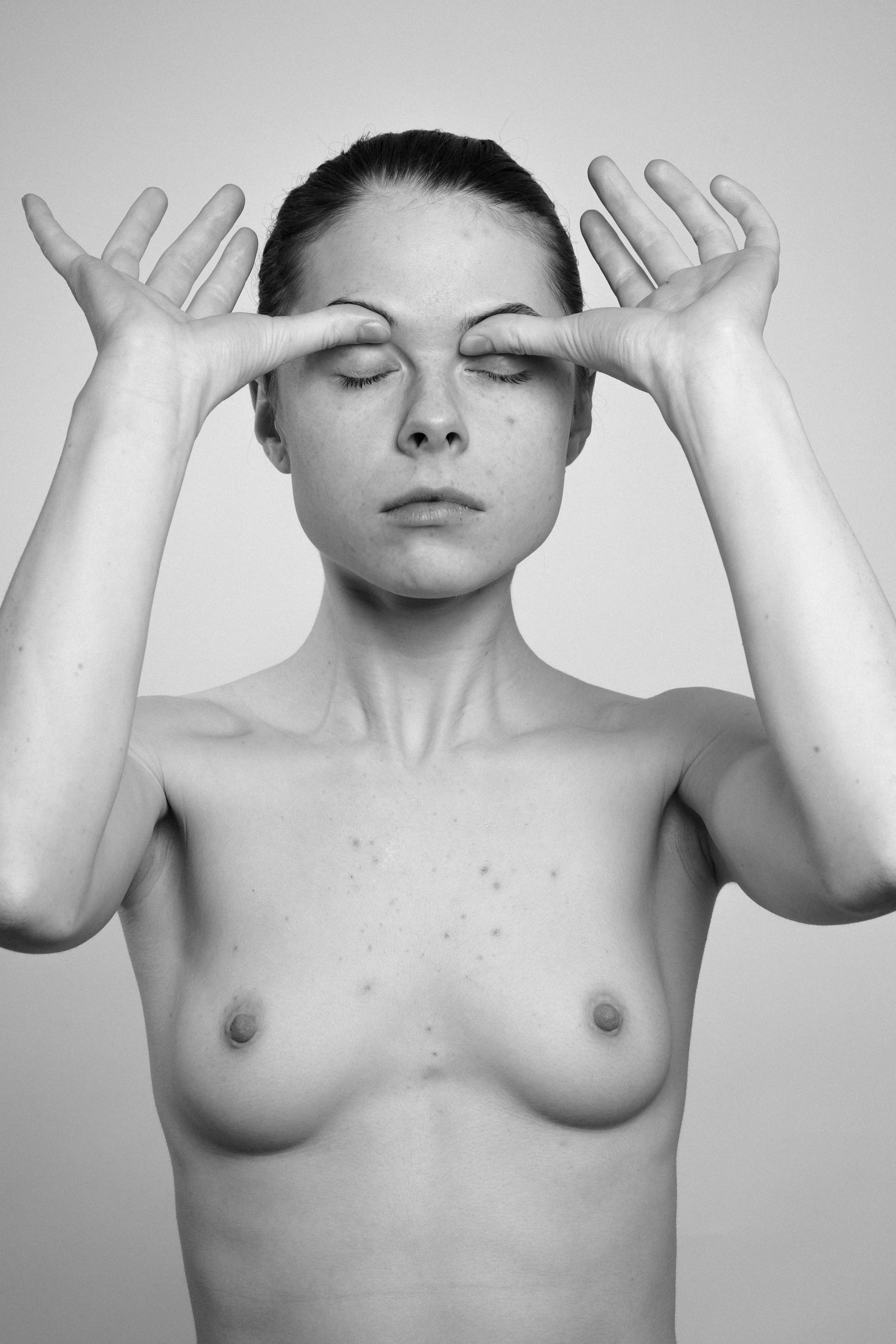 Studio portrait of a young woman in black and white. She manipulates her face, stretches her skin, with her both hands, makes faces, grimaces.