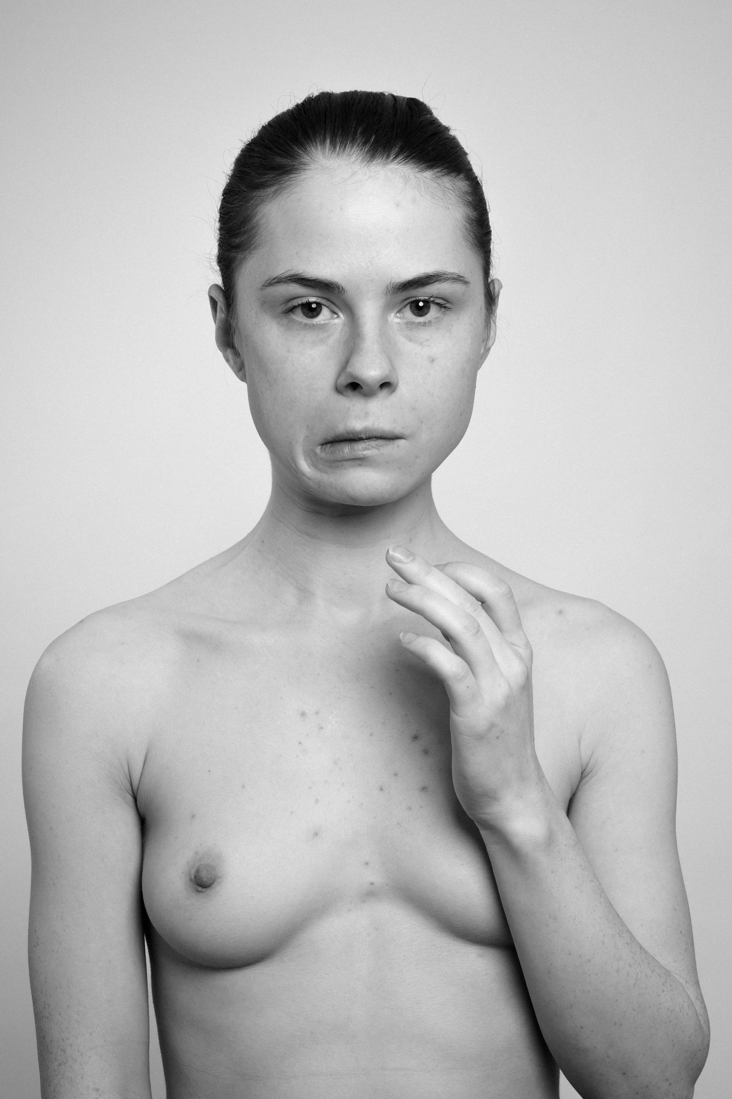 Studio portrait of a young woman in black and white. She manipulates her face, makes faces, grimaces.