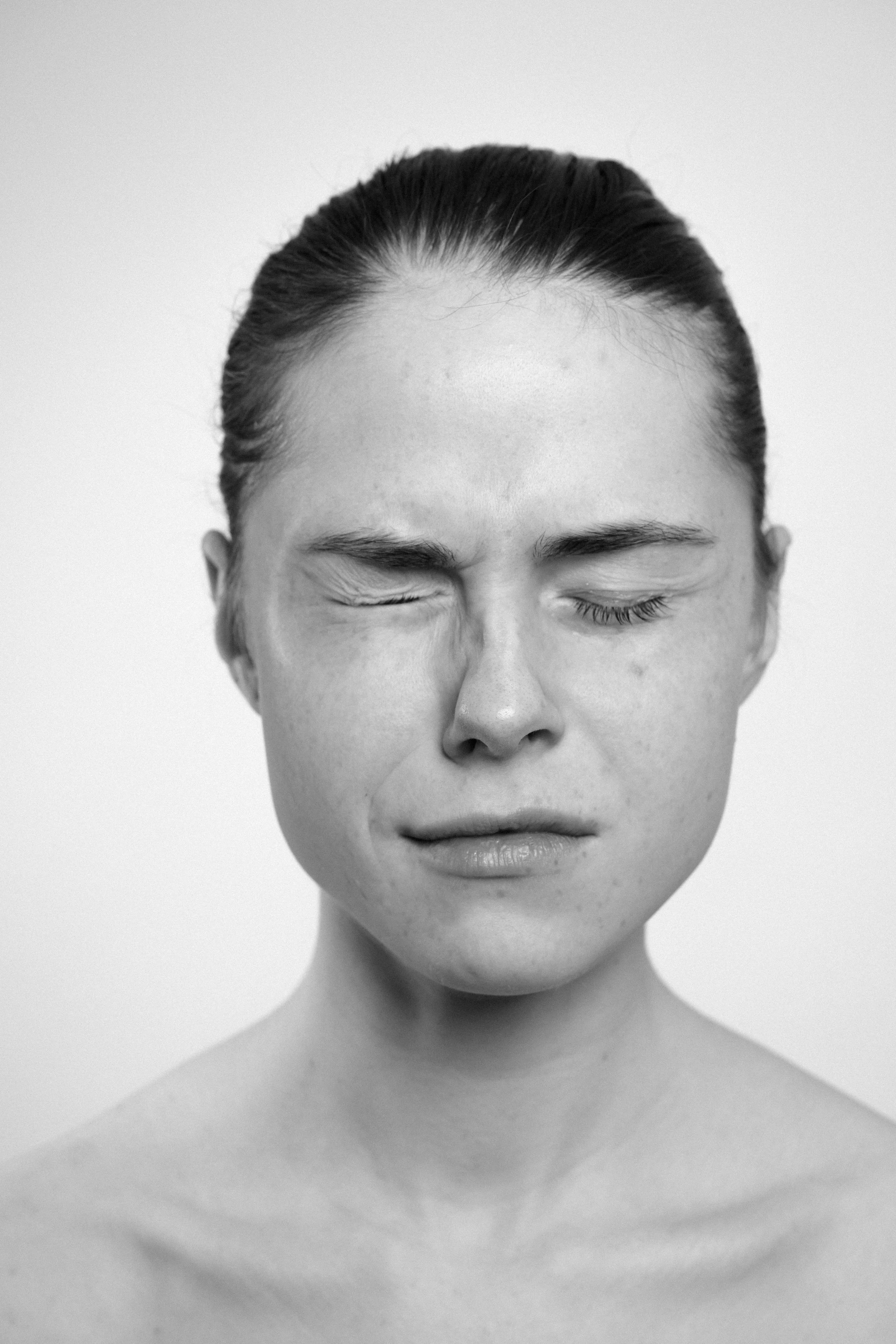 Studio portrait of a young woman in black and white. She frowns, makes faces, grimaces, as if in pain.