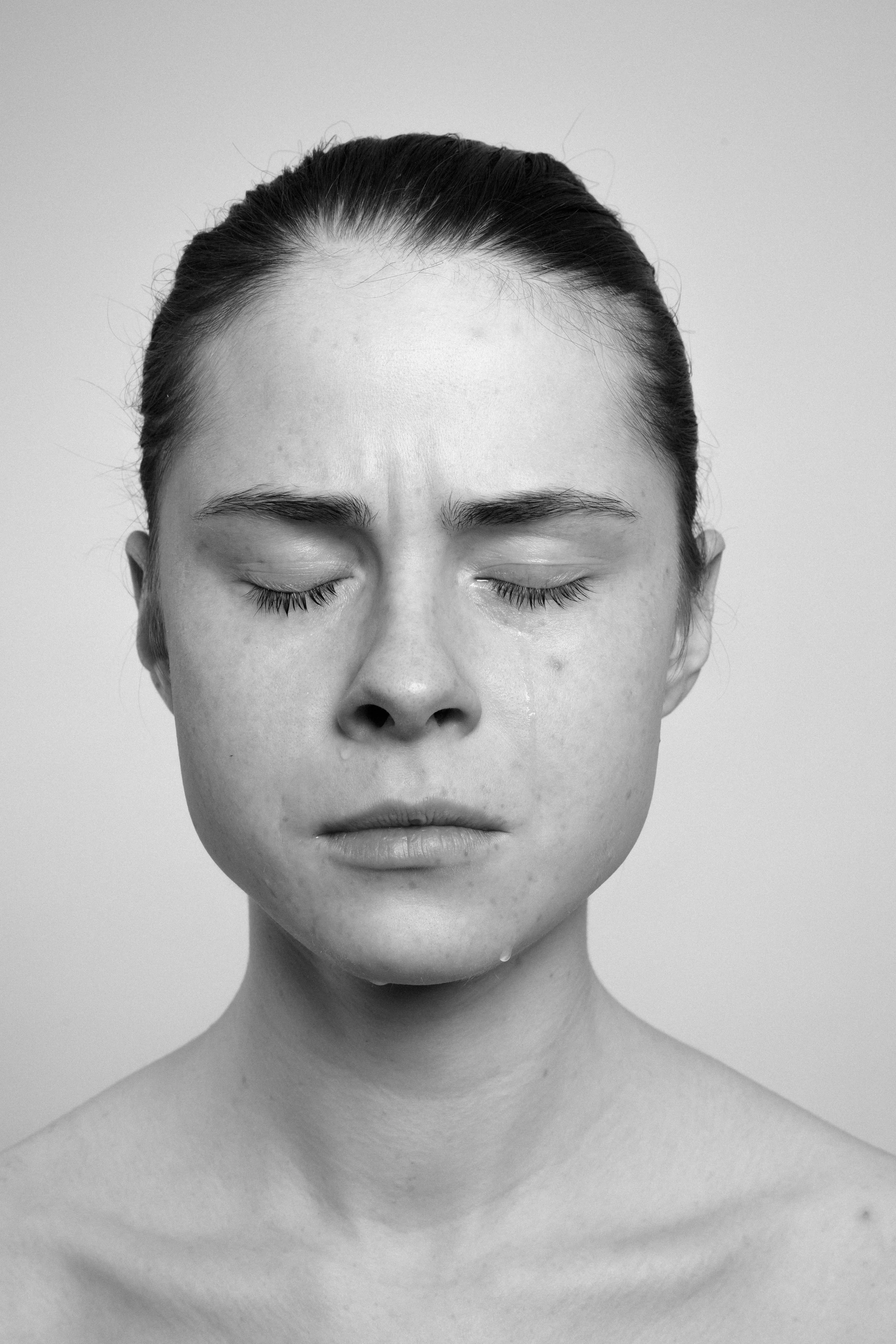 Studio portrait of a young woman in black and white. She frowns, makes faces, grimaces, as if in pain.