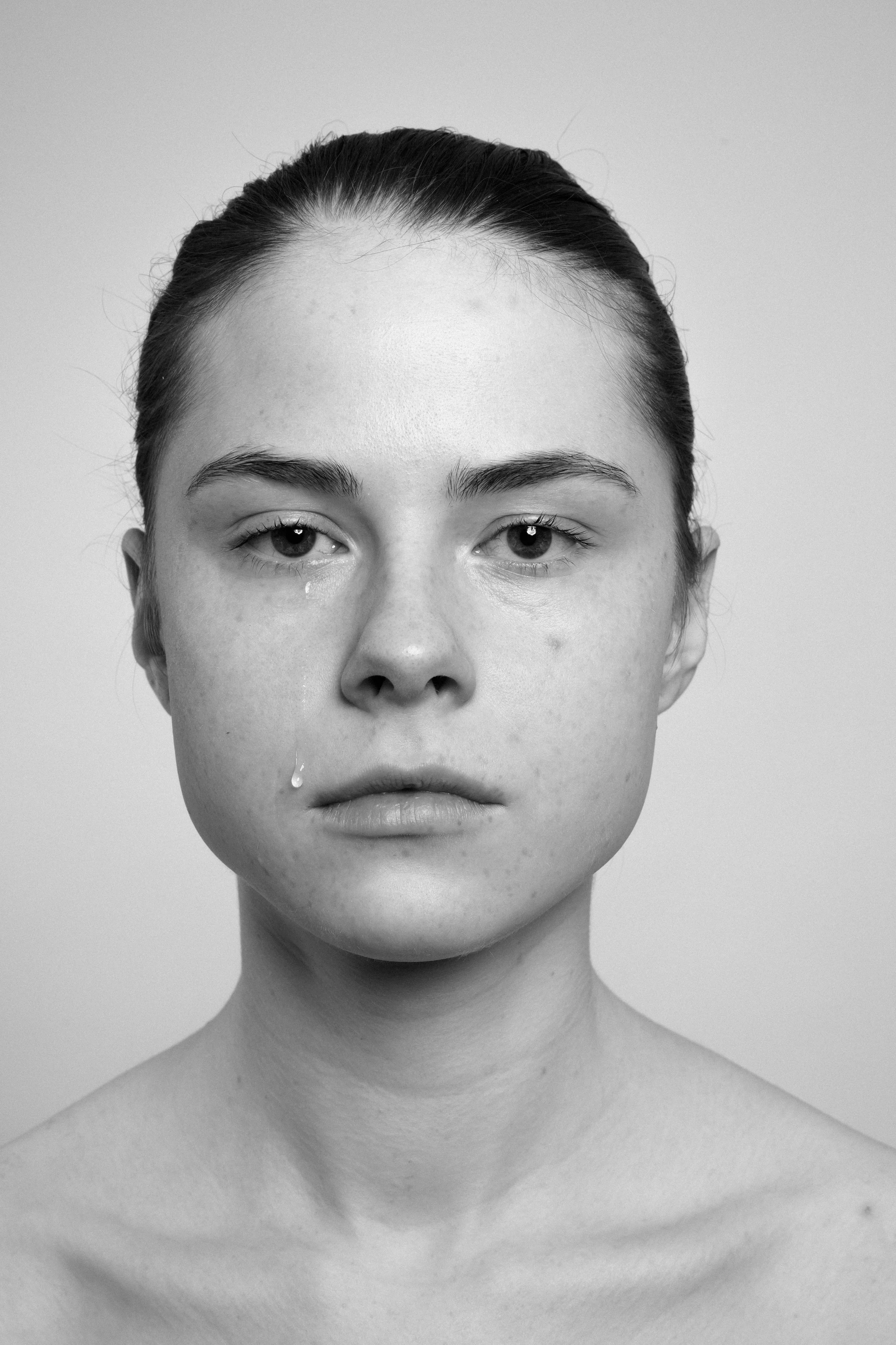 Studio portrait of a young woman in black and white. She is crying, her tears show up.