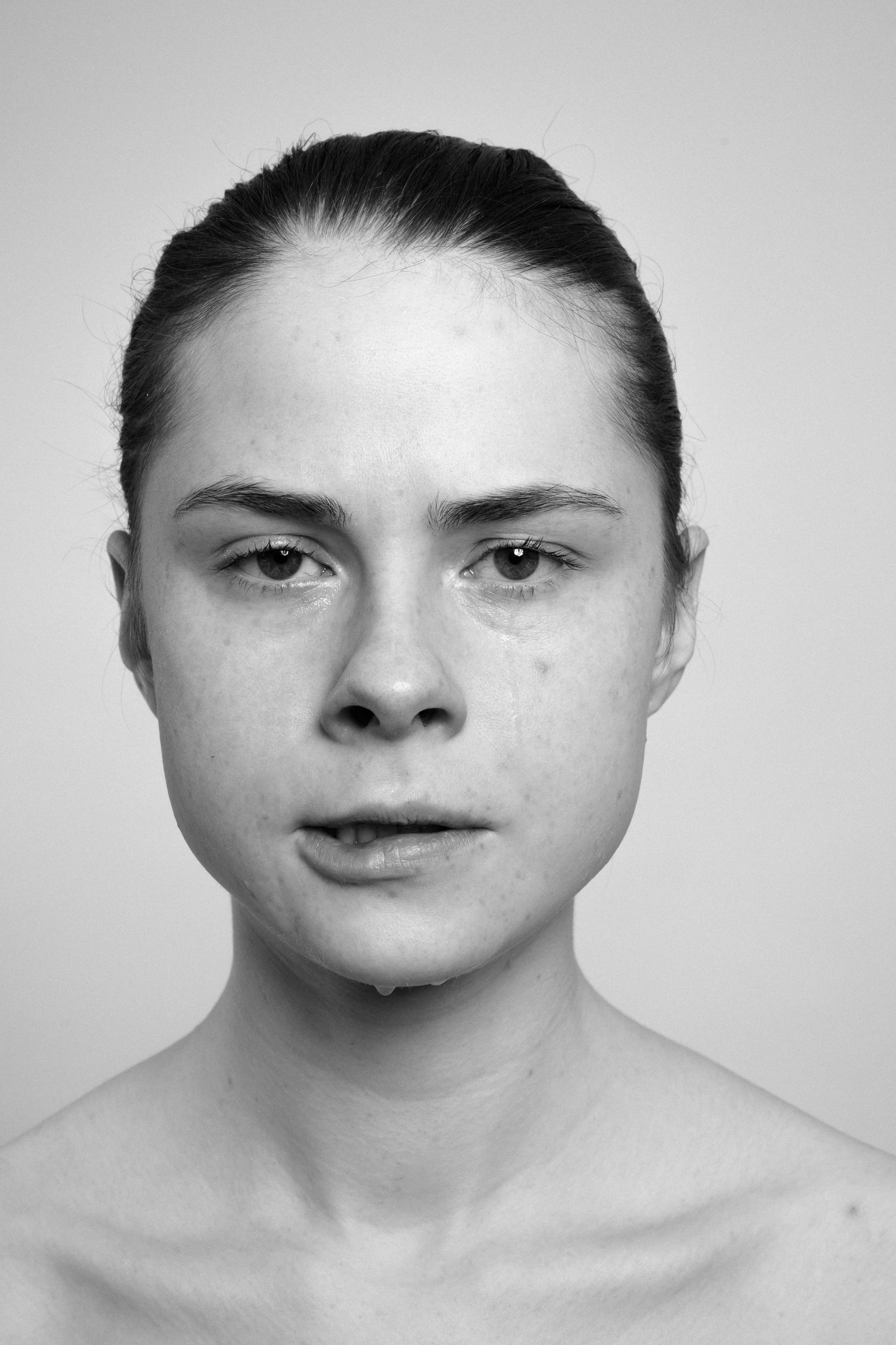 Studio portrait of a young woman in black and white. She makes faces, grimaces, looks concerned.