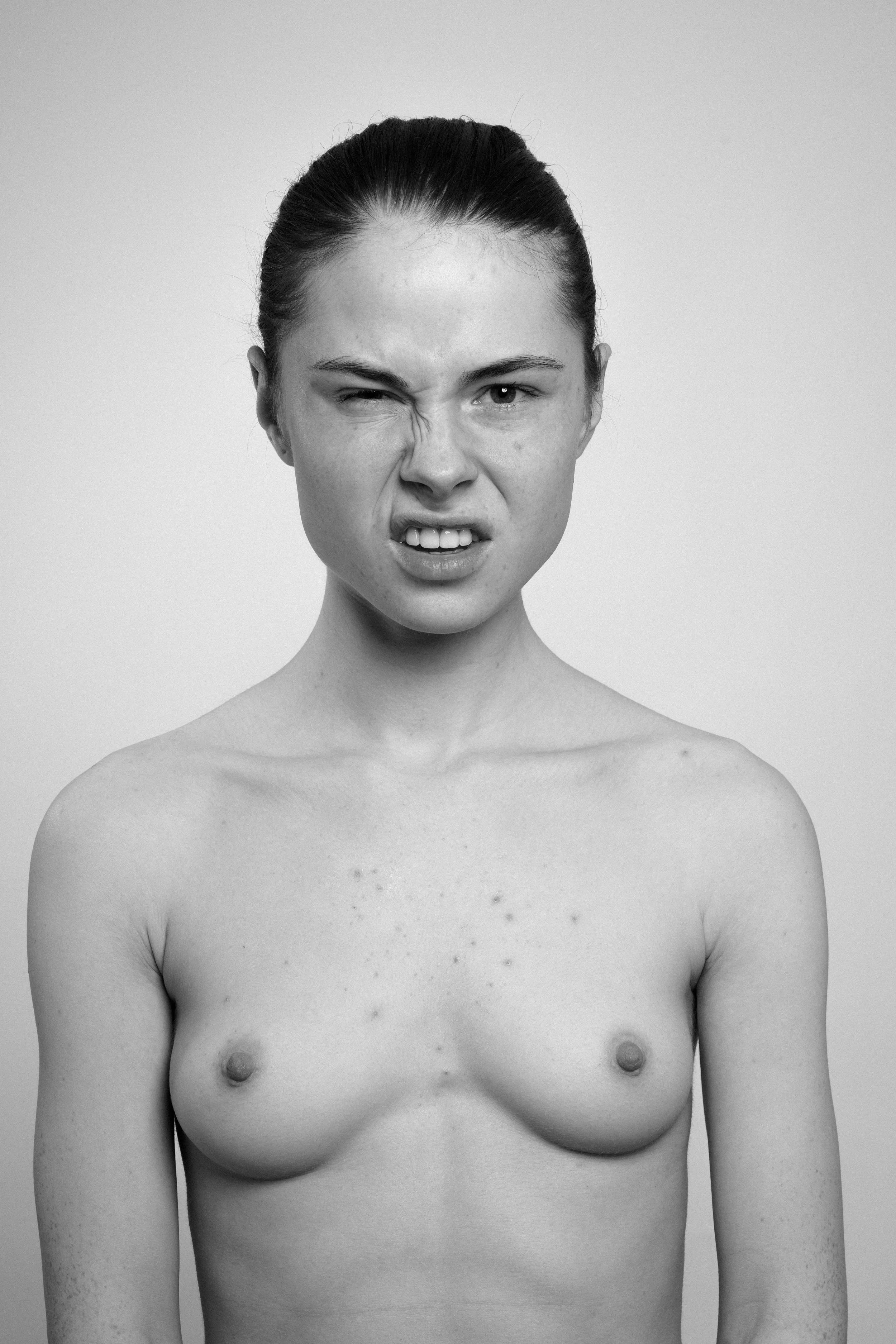 Studio portrait of a young woman in black and white. She makes faces, grimaces and shows her teeth.