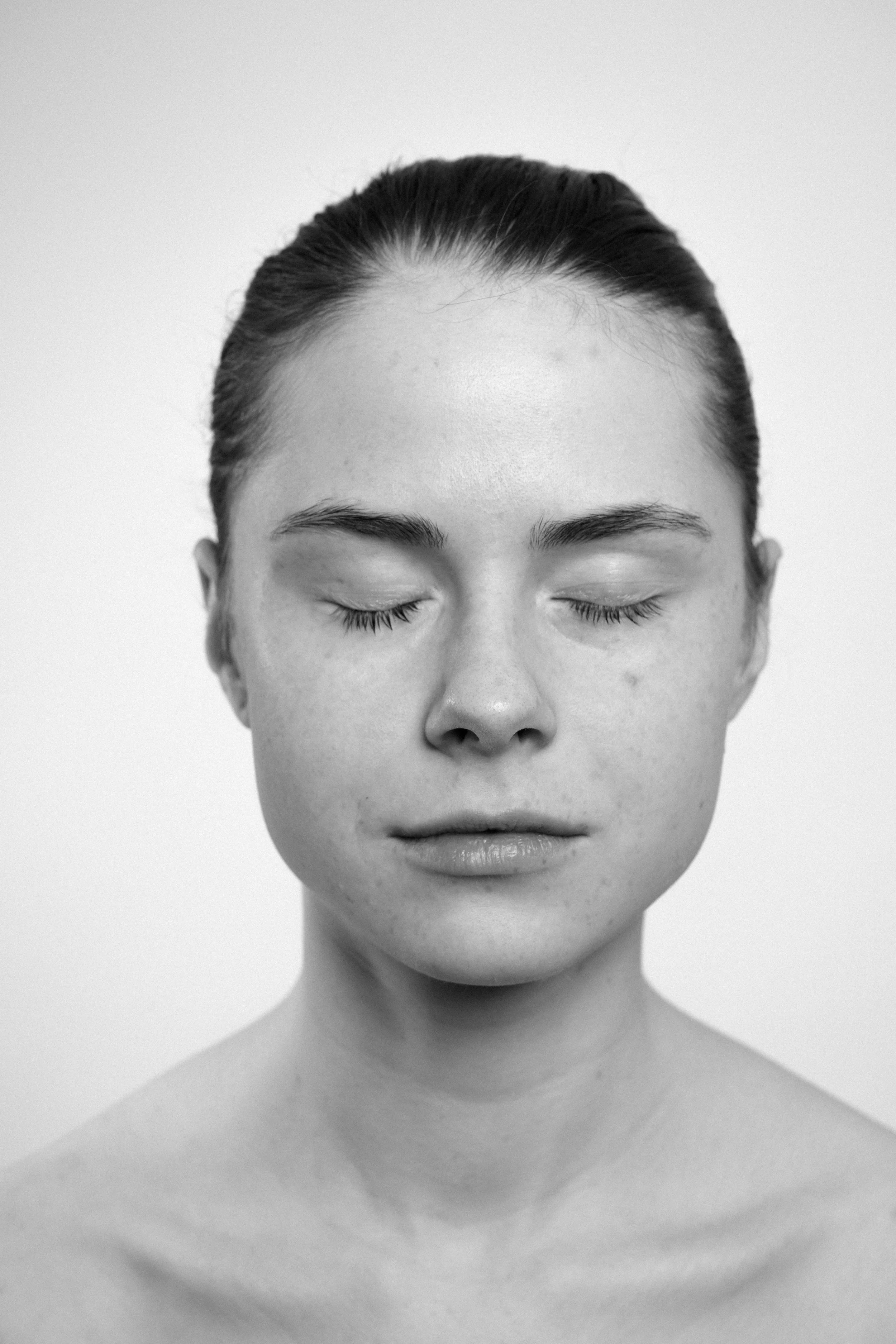 Studio portrait of a young woman in black and white. She has a peaceful facial expression. Both her eyes are closed.