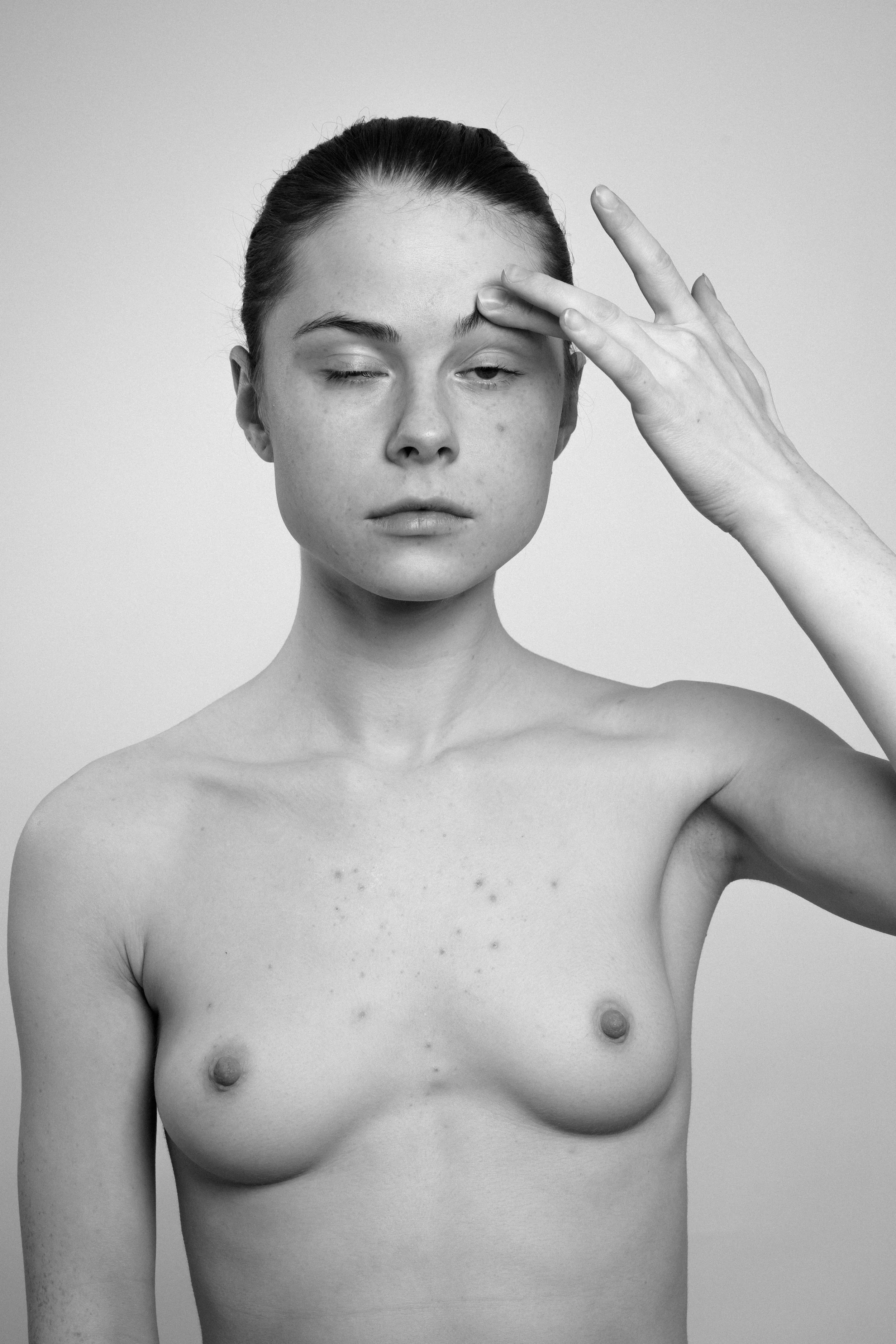 Studio portrait of a young woman in black and white. She manipulates touches her forehead with her left hand, makes faces, grimaces.