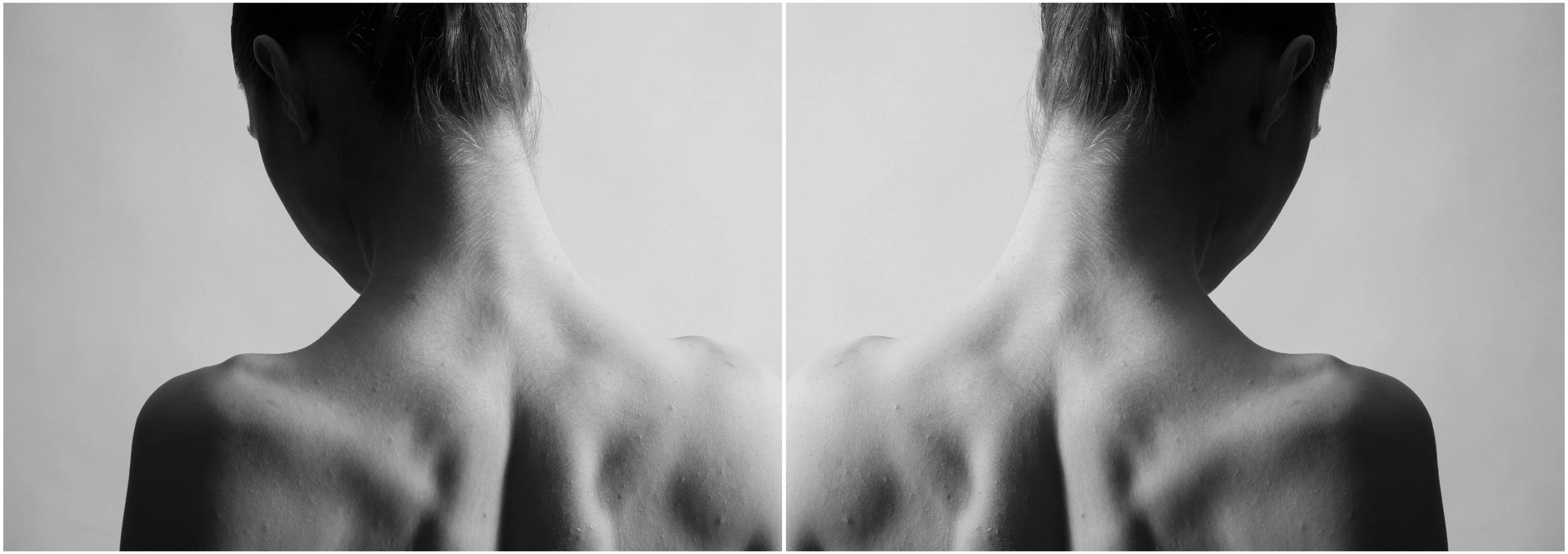 A black and white mirror-reflection photographic portrait of a young woman. A close-up, cropped portait showing her muscular back in tension. Very strong shadows and contrasts.