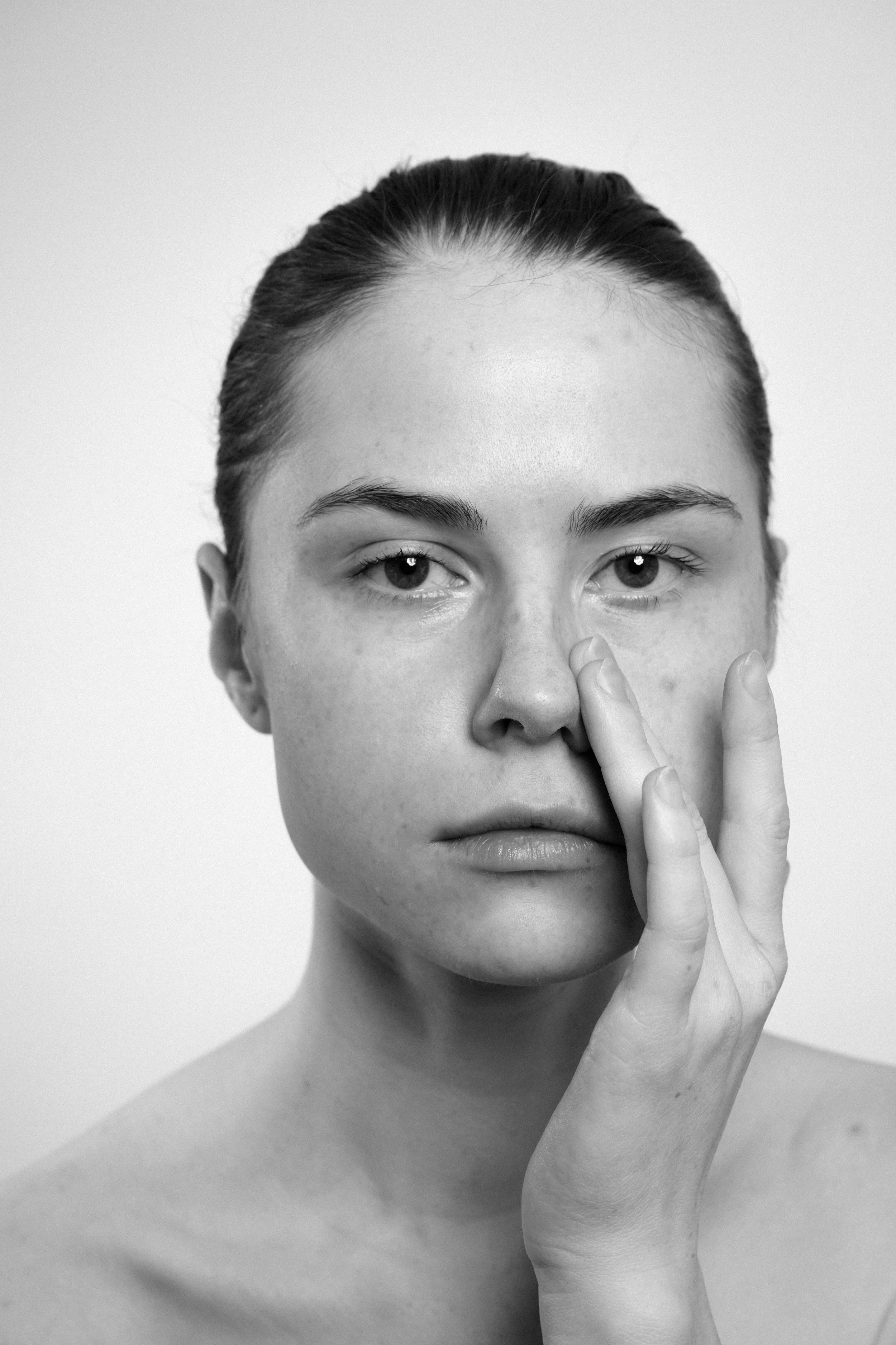 Studio portrait of a young woman in black and white. She touches her face with her left hand.
