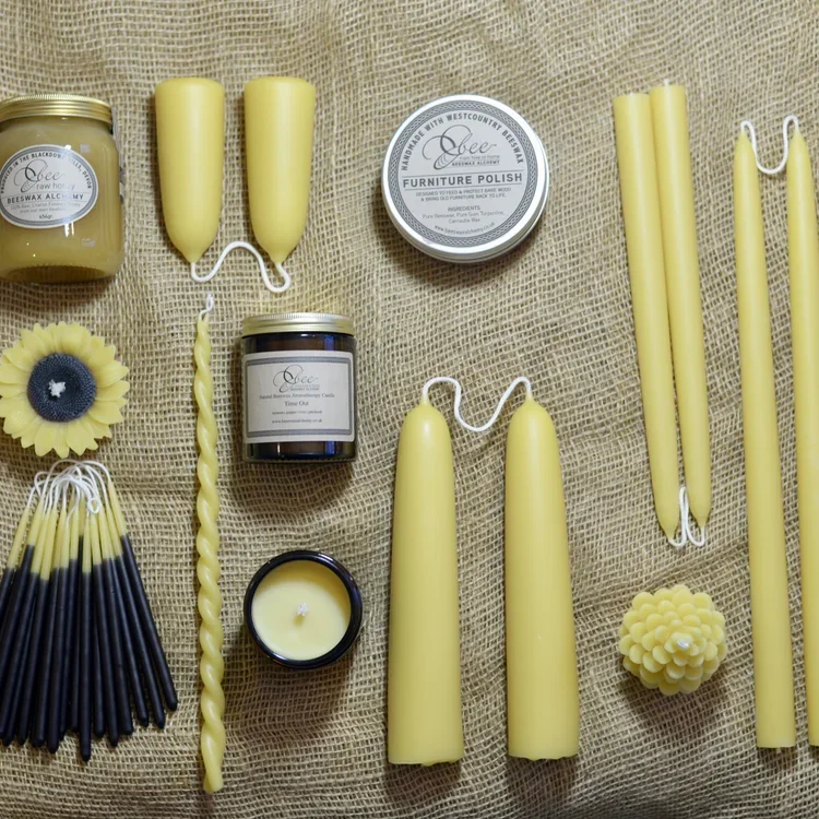 Assorted yellow candles, a jar of furniture polish, a container of wax, a wax flower, and a wax candle in various shapes on a burlap surface.