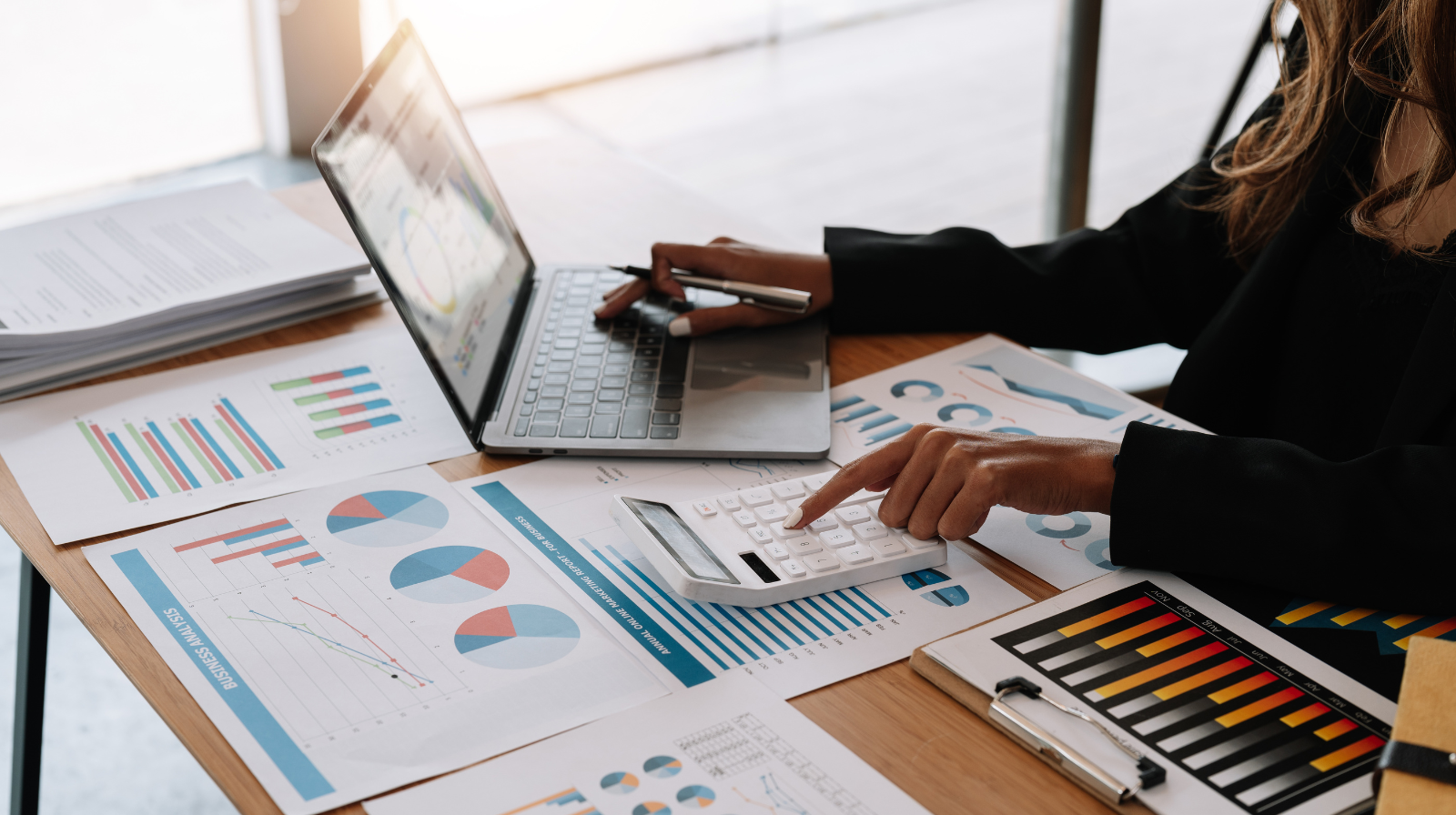 Person working with financial charts, graphs, and a calculator on a wooden desk.