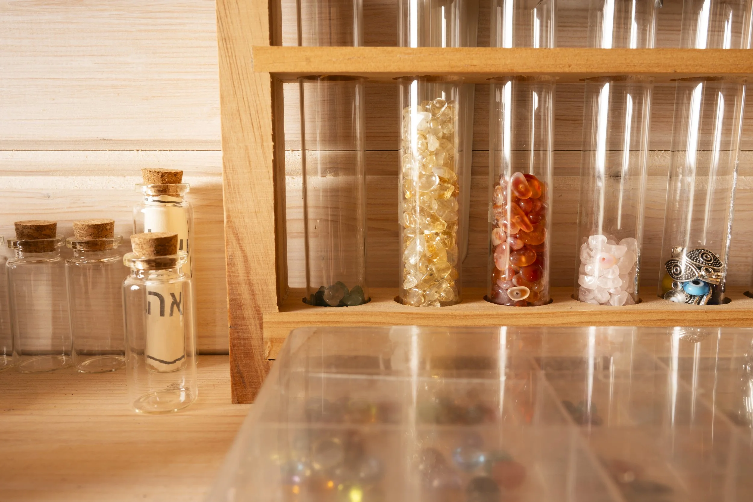 Glass vials with cork stoppers and a wooden shelf containing test tubes filled with colorful beads or stones, set against a wooden background.
