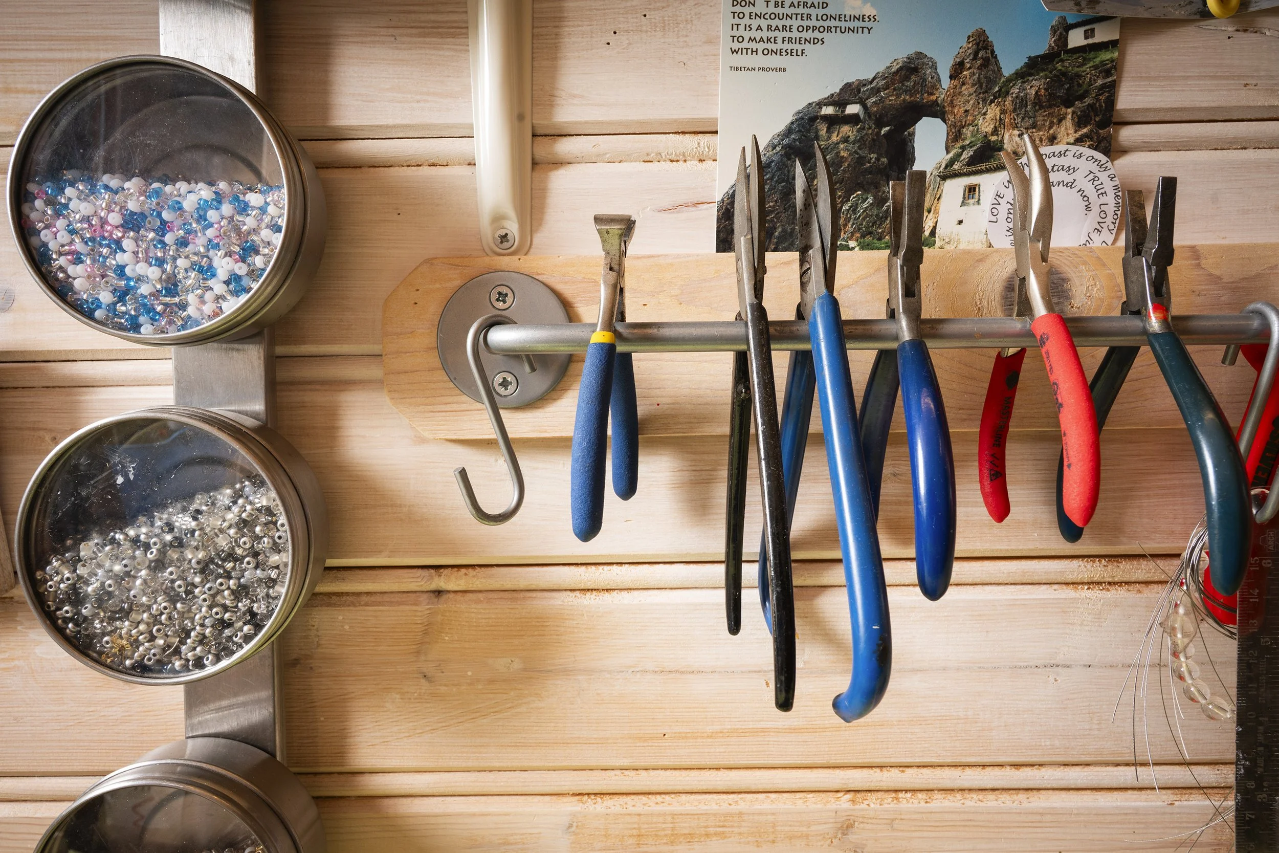 A wall-mounted jewelry making station with pliers and beading supplies, including bowls of mixed beads and a wooden pegboard with hooks