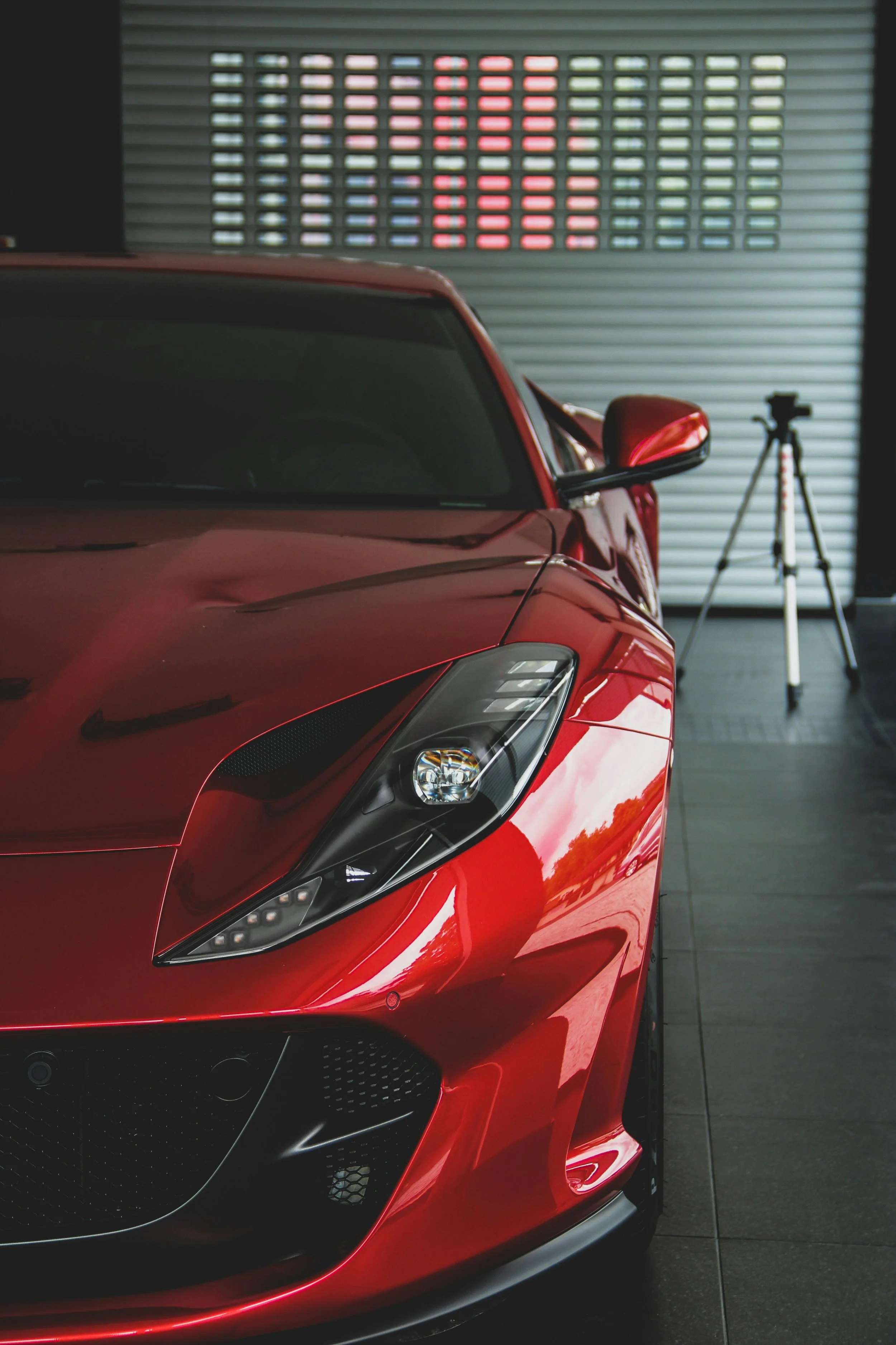 Red sports car inside a garage with a tripod in the background.