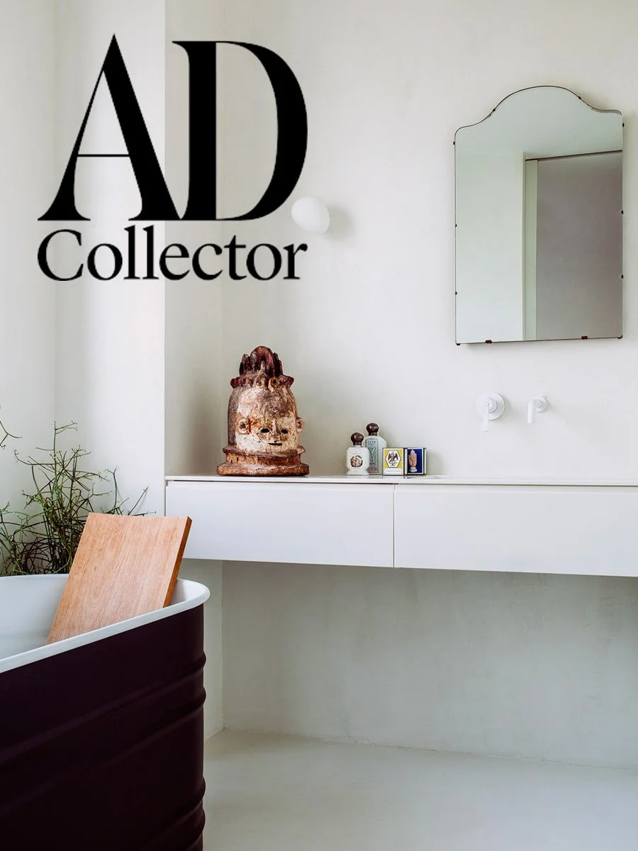 Vue d'un intérieur minimaliste avec un miroir, une console blanche, une sculpture ancienne, des petites bouteilles, et un miroir rectangulaire sans cadre à gauche.