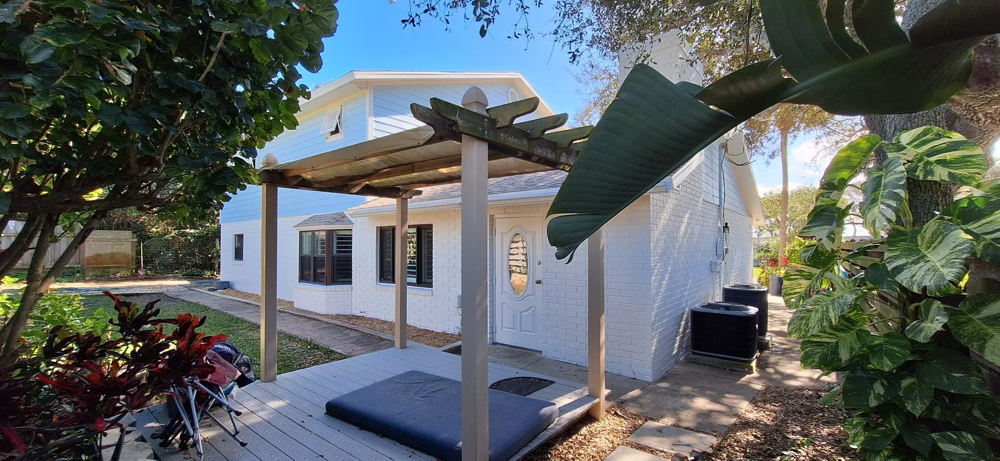 Backyard view featuring white painted brick, pergola structure, and lush Florida landscaping in New Smyrna Beach.