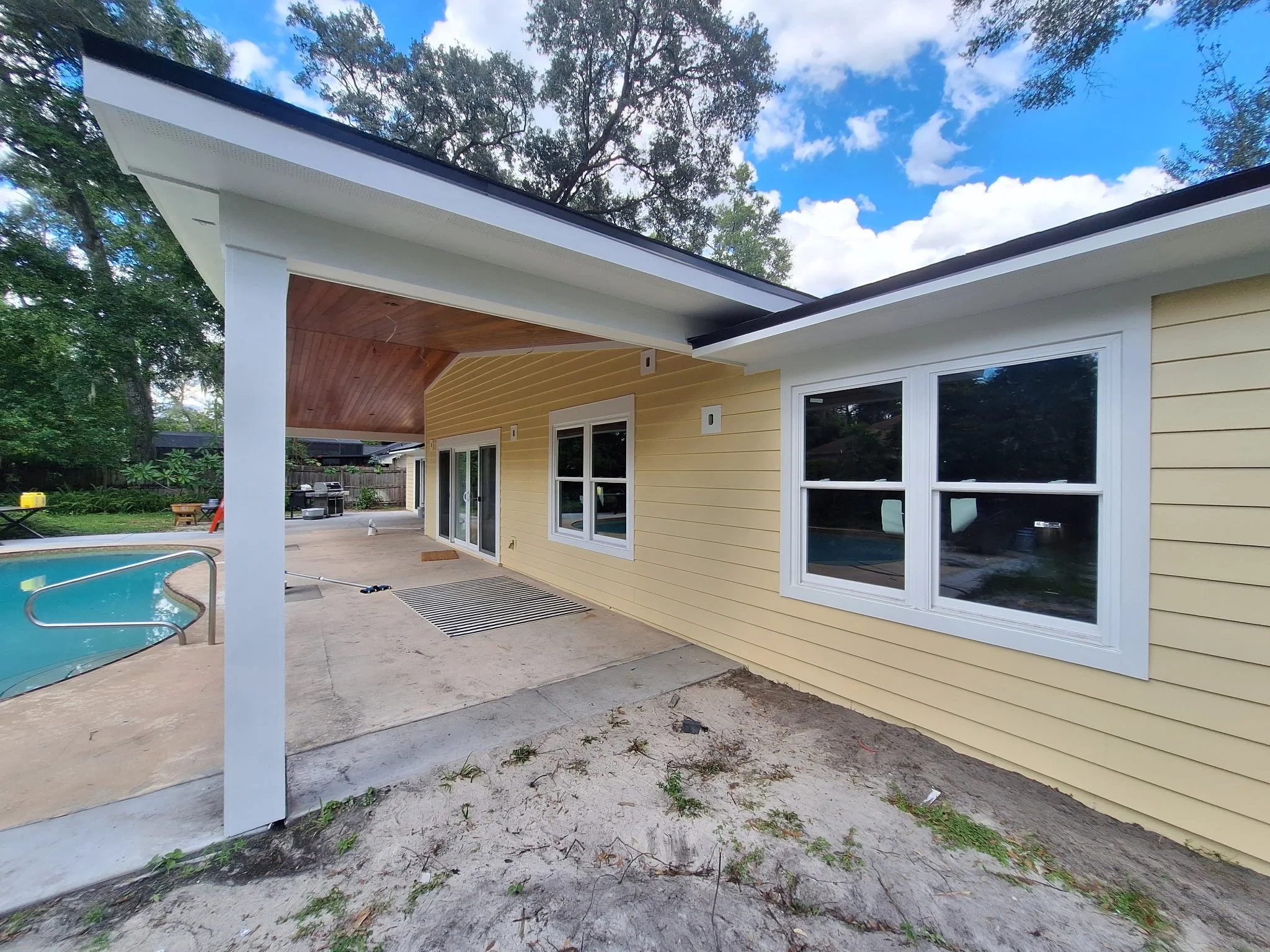 Backyard exterior painting project in Longwood FL featuring sunny yellow siding, white trim, covered patio, and pool area