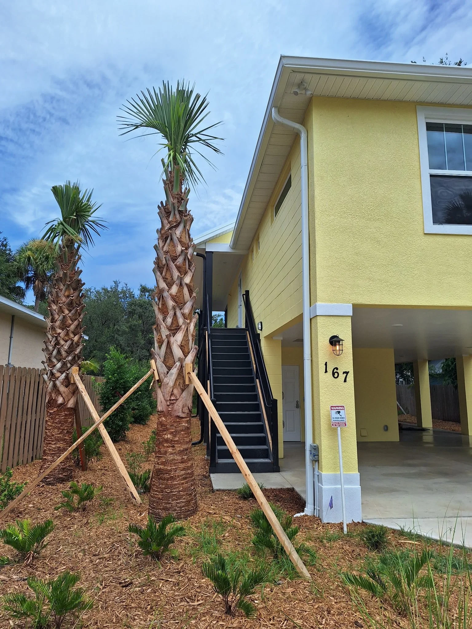 Front exterior of yellow canal home in New Smyrna Beach with palm trees and stairs