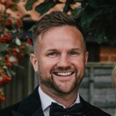 Smiling man with short hair and beard in a black tuxedo at a formal event