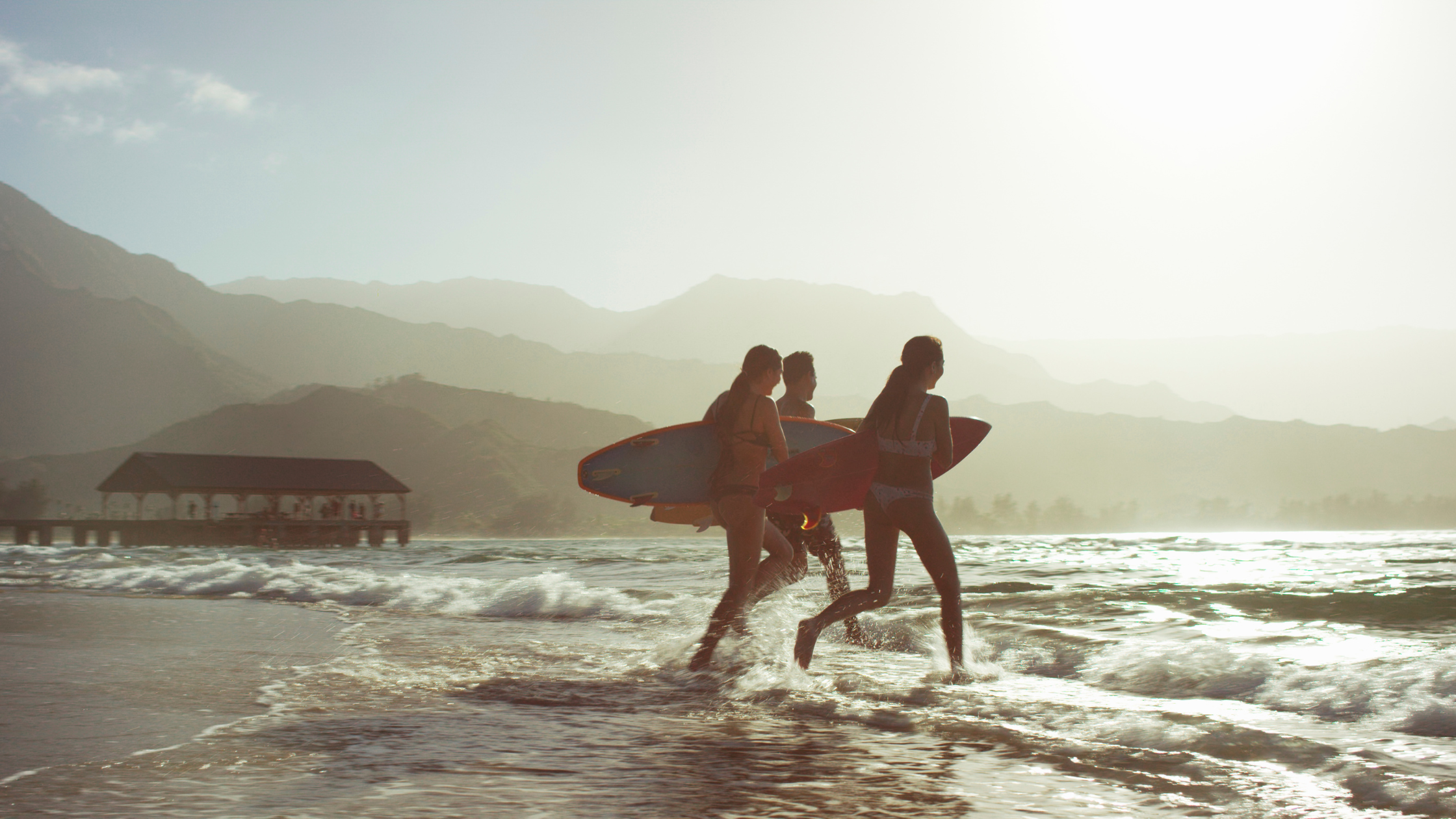 Surfers running on the beach with their boards, symbolising freedom and protection through insurance